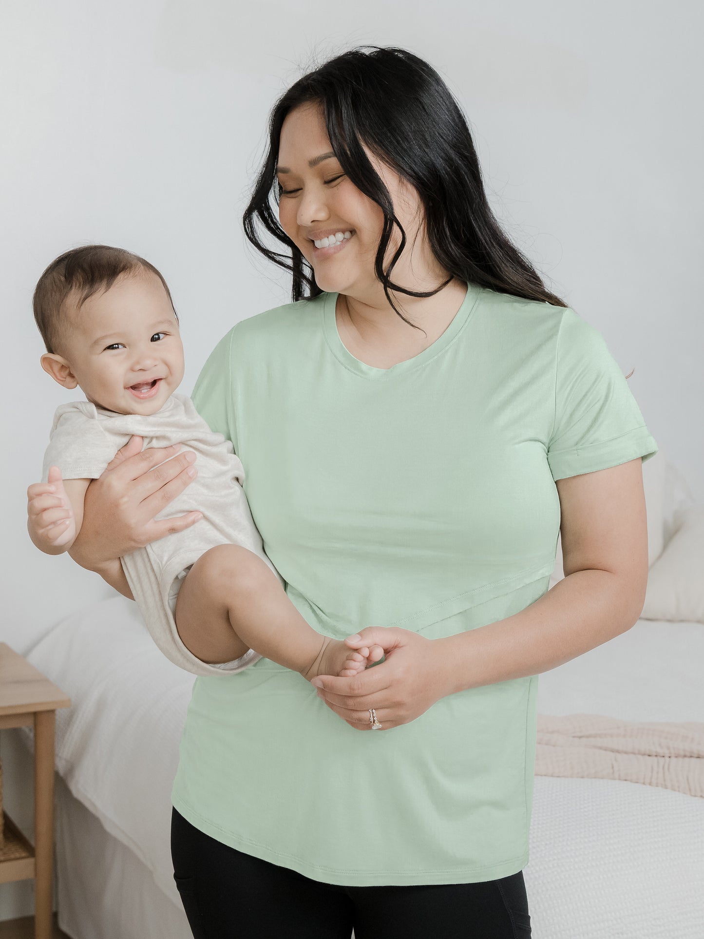 Model wearing the Everyday Asymmetrical Nursing T-shirt in Soft Mint with her baby on her hip.