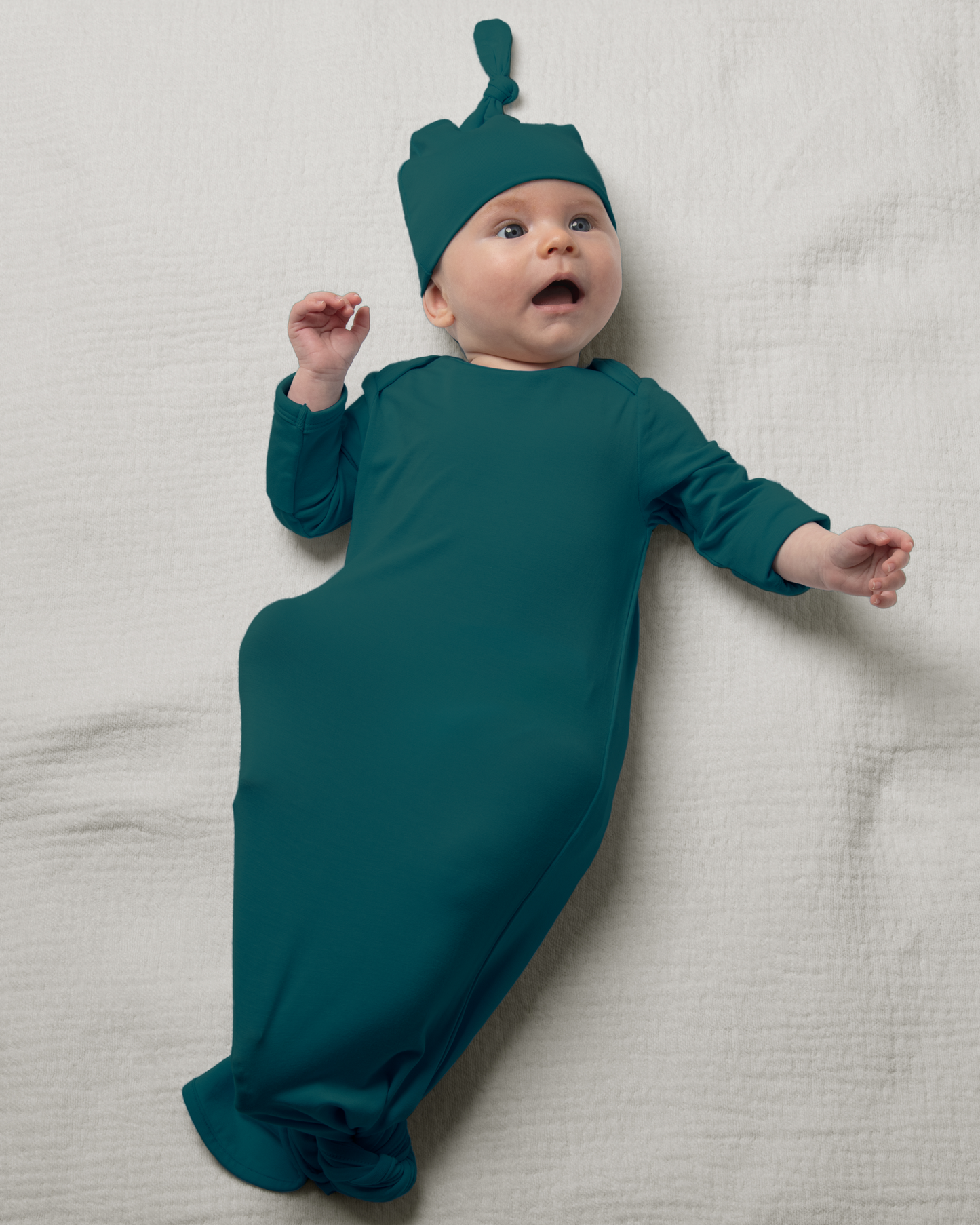 Baby in Bamboo Knotted Baby Gown in Evergreen lying on a light gray surface@model_info:Danny is 3 months old.