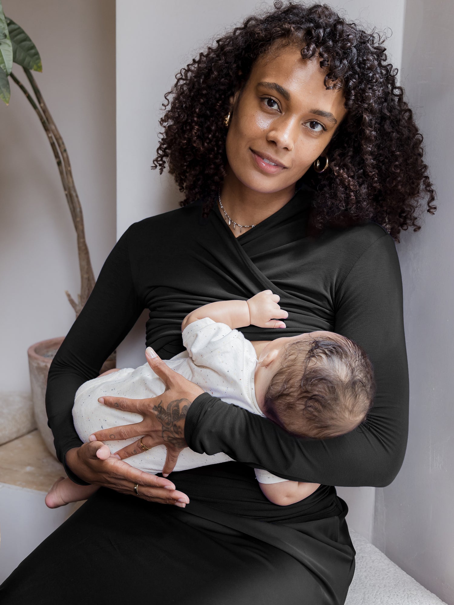 Model wearing the Gianna Shirred Maternity & Nursing Top in Black sitting and nursing baby