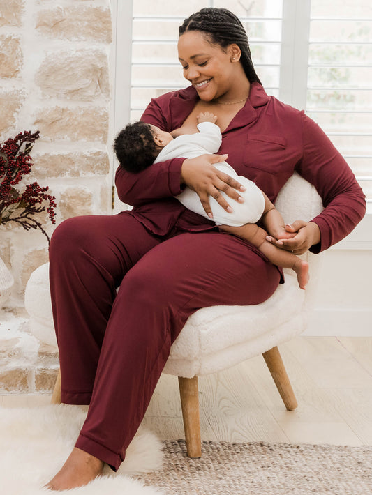 Model wearing the Clea Bamboo Long Sleeve Pajama Set in Fig feeding her baby.