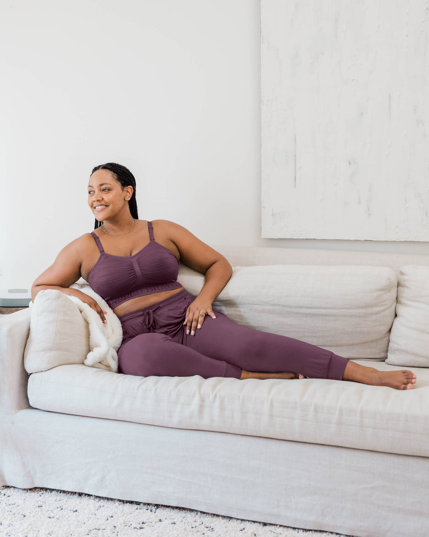 Model lounging on sofa wearing the Everyday Lounge Jogger in Burgundy Plum, paired with matching Sublime® Hands-Free Pumping & Nursing Bra @model_info:Roxanne is 5'9" and wearing a Large Regular.