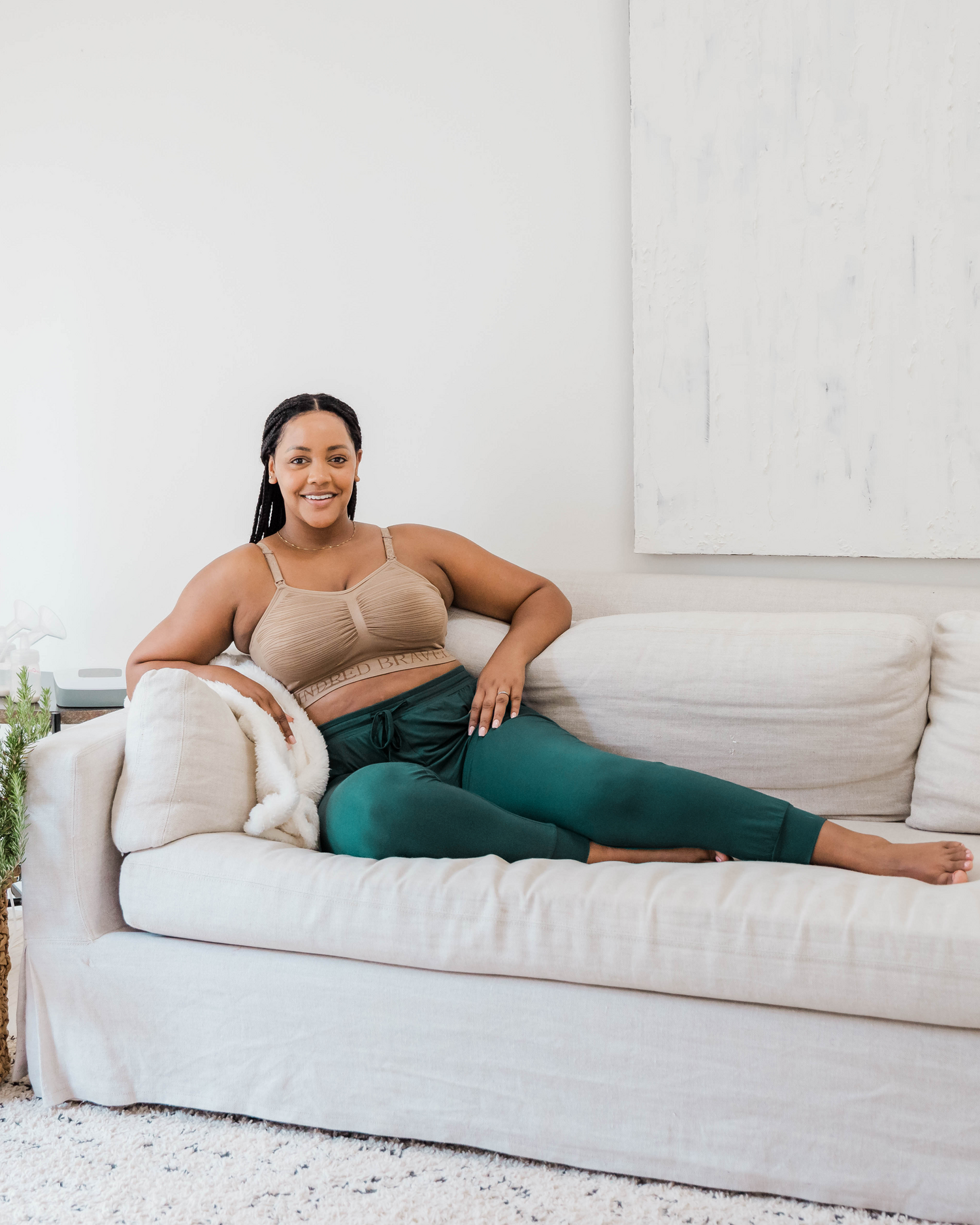 Model lounging on sofa wearing the Everyday Lounge Jogger in Evergreen, paired with the Sublime® Hands-Free Pumping & Nursing Bra in Latte@model_info:Roxanne is 5'9" and wearing a Large Regular.