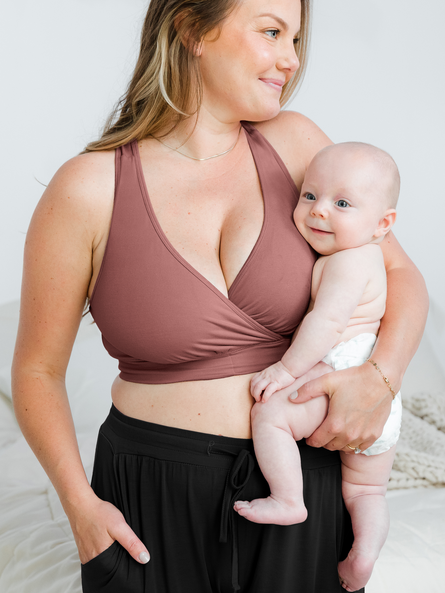 Model wearing the French Terry Nursing Bra in Redwood and holding her smiling infant.@model_info:Ali is wearing a Large Busty.