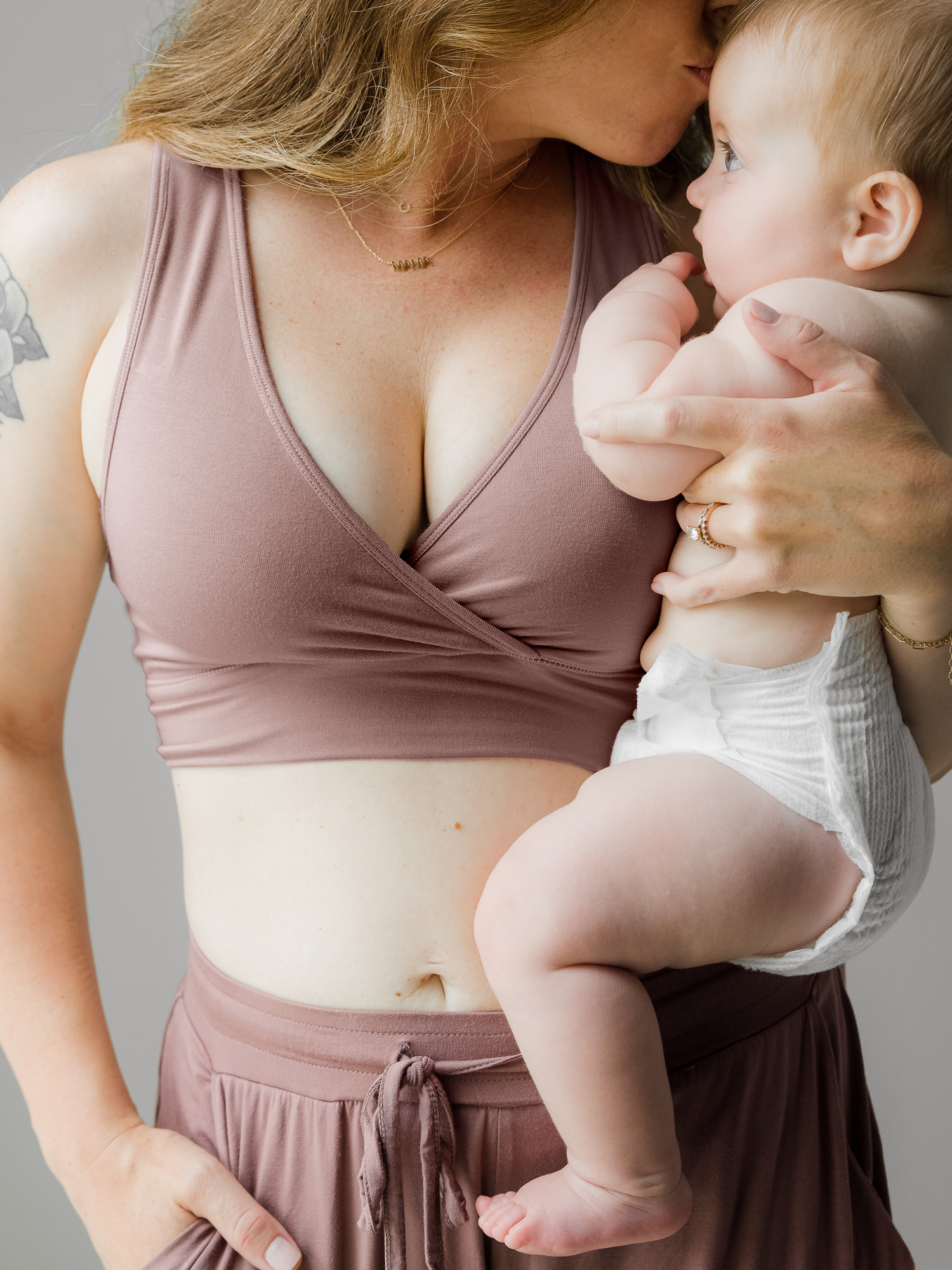 Model holding her baby and giving him a kiss. She wears the French Terry Nursing Bra in Twilight and the Everyday Joggers in Twilight. @model_info:Ashley is wearing a Small.