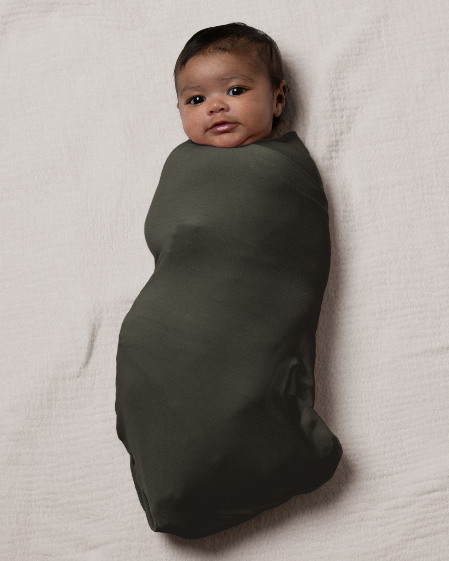Baby wrapped in Bamboo Swaddle Blanket in Thyme on a light beige blanket@model_info:Luna is 6 weeks old.