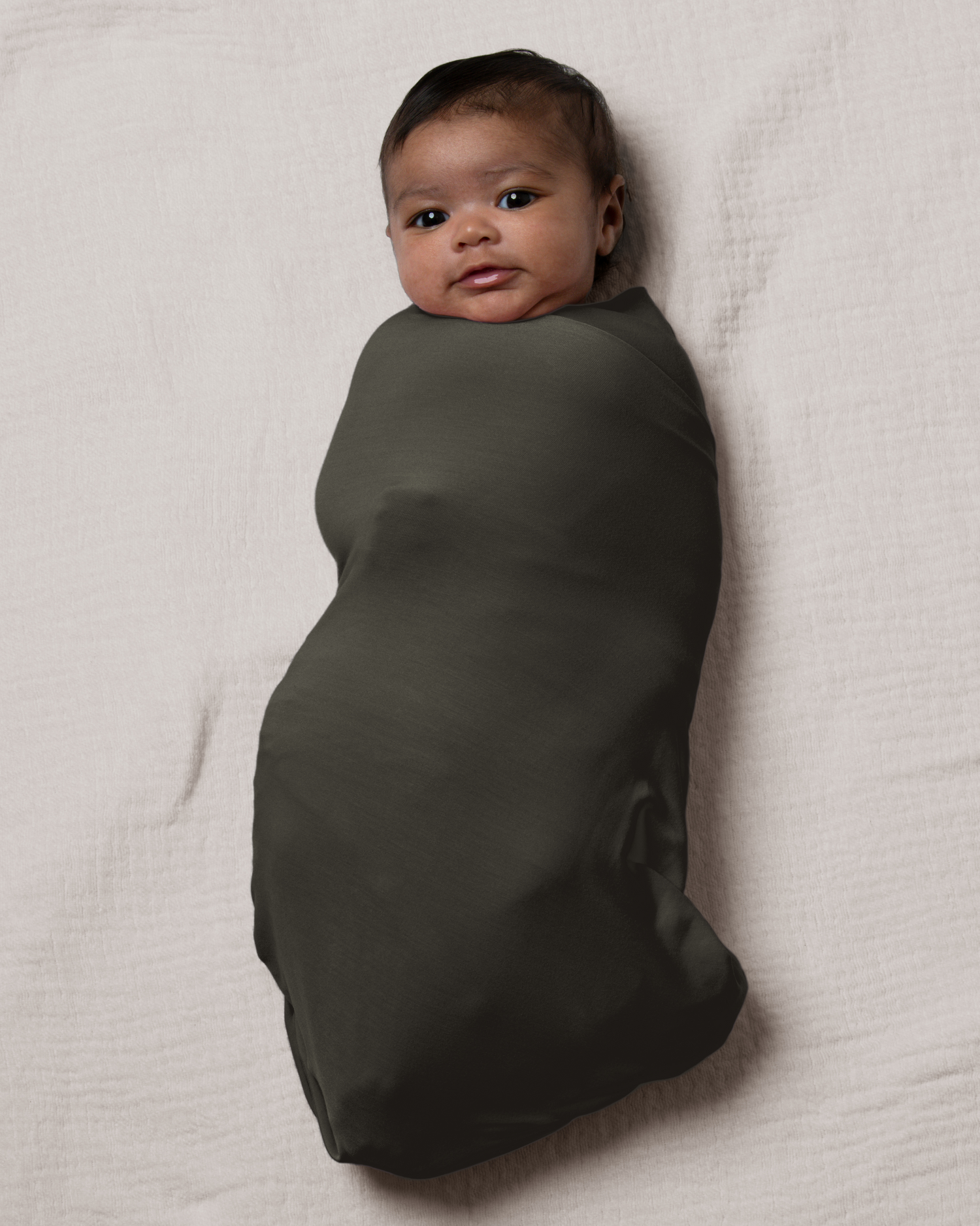 Baby wrapped in Bamboo Swaddle Blanket in Thyme on a light beige blanket@model_info:Luna is 6 weeks old.