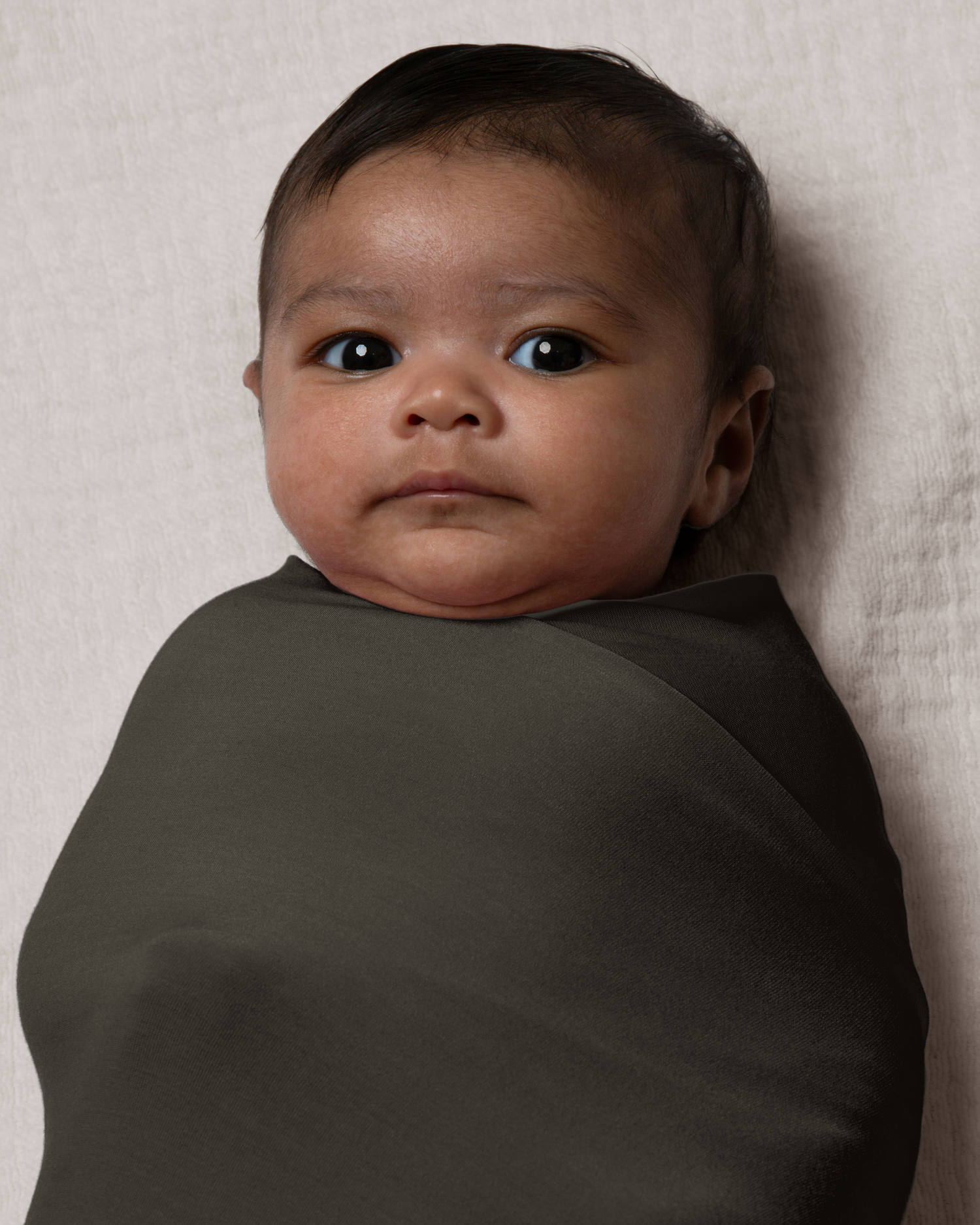 Baby wrapped in Bamboo Swaddle Blanket in Thyme against a light background