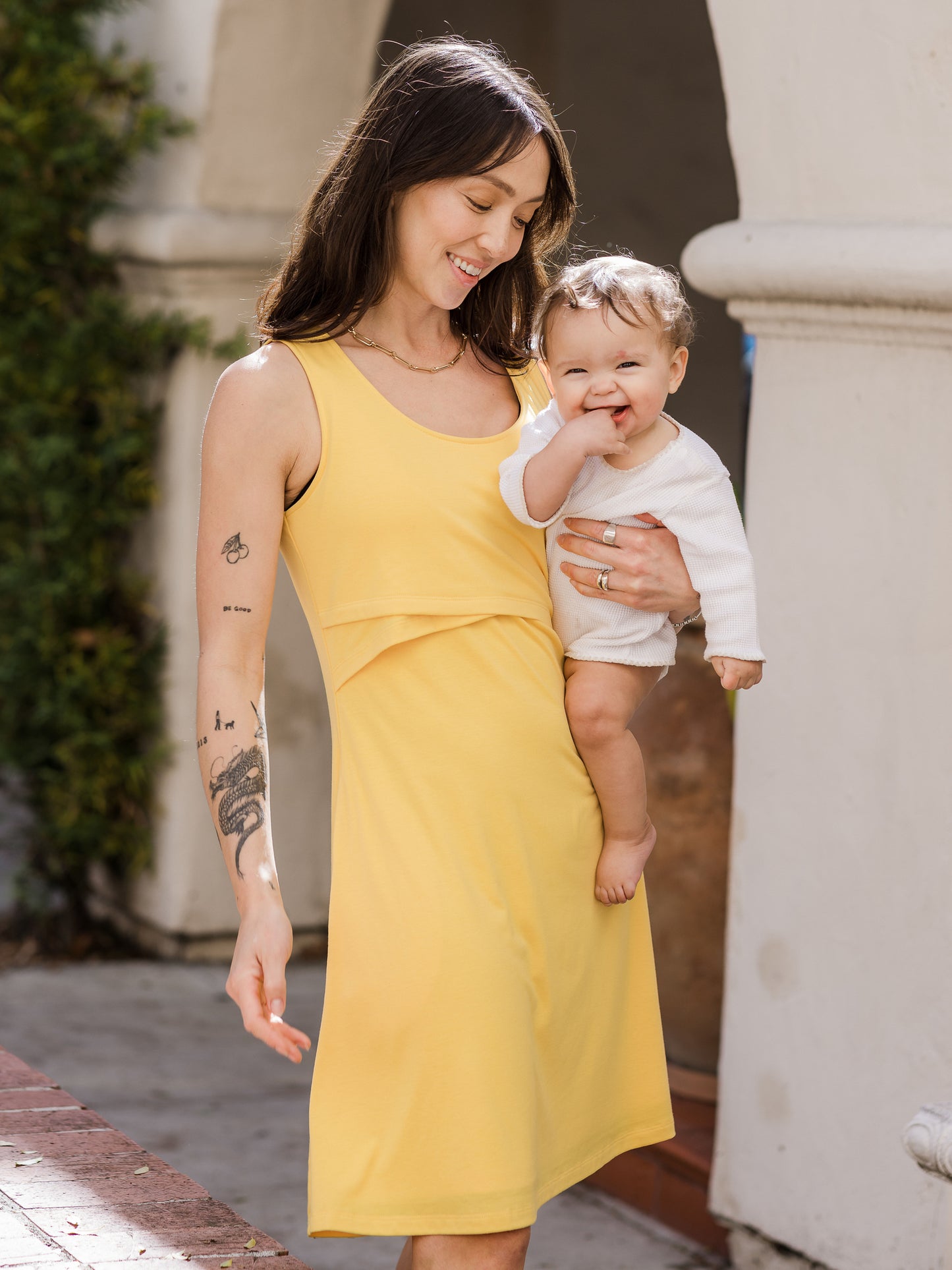 Front view of model wearing the Penelope Crossover Nursing Dress in citrus, holding baby