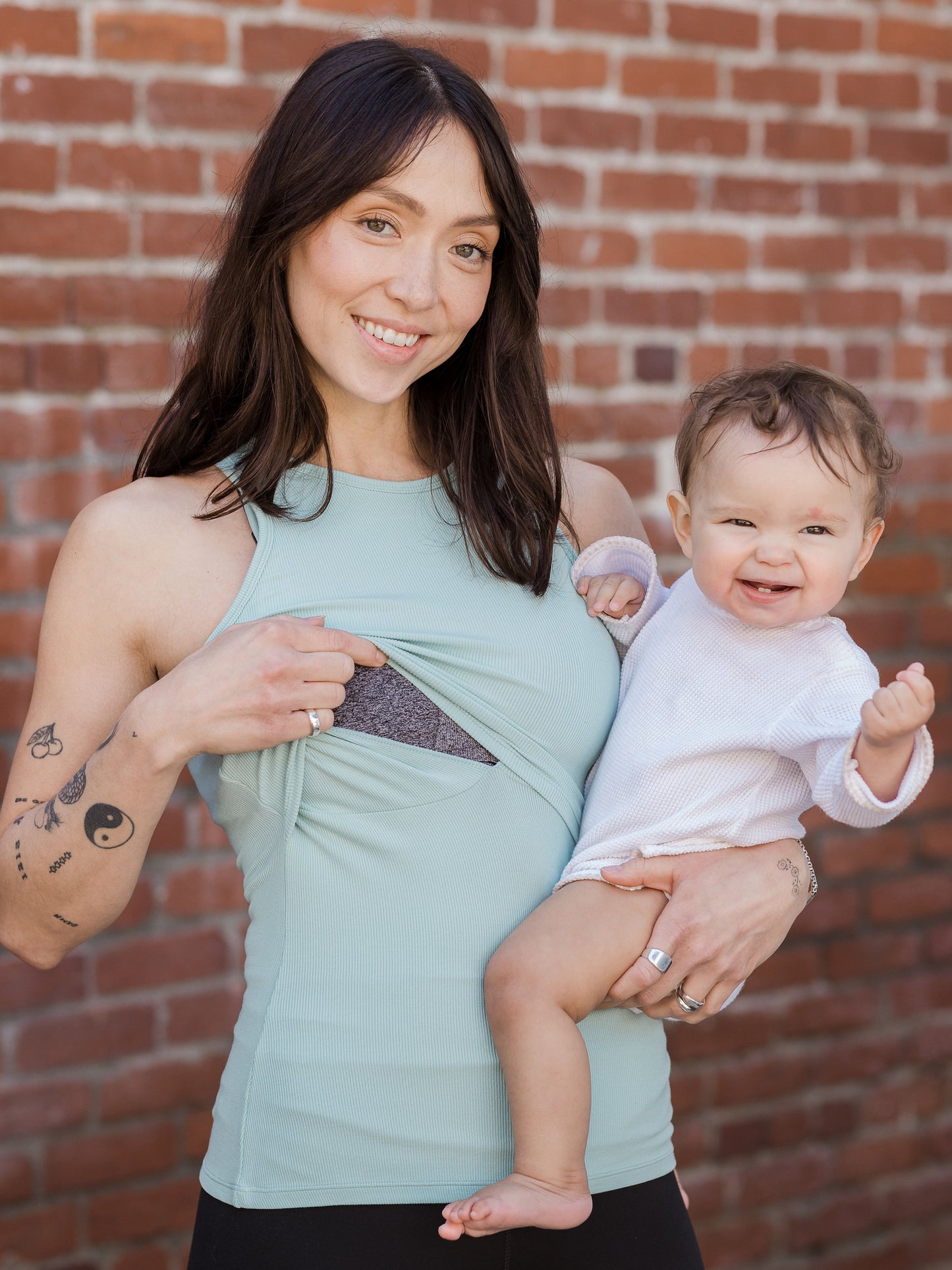 Model holding baby and showing nursing access on the Ribbed Bamboo Racerback Nursing Tank in dusty blue green 