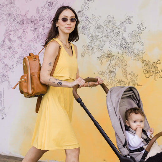 Model wearing yellow Penelope Nursing Dress and pushing her baby in a stroller