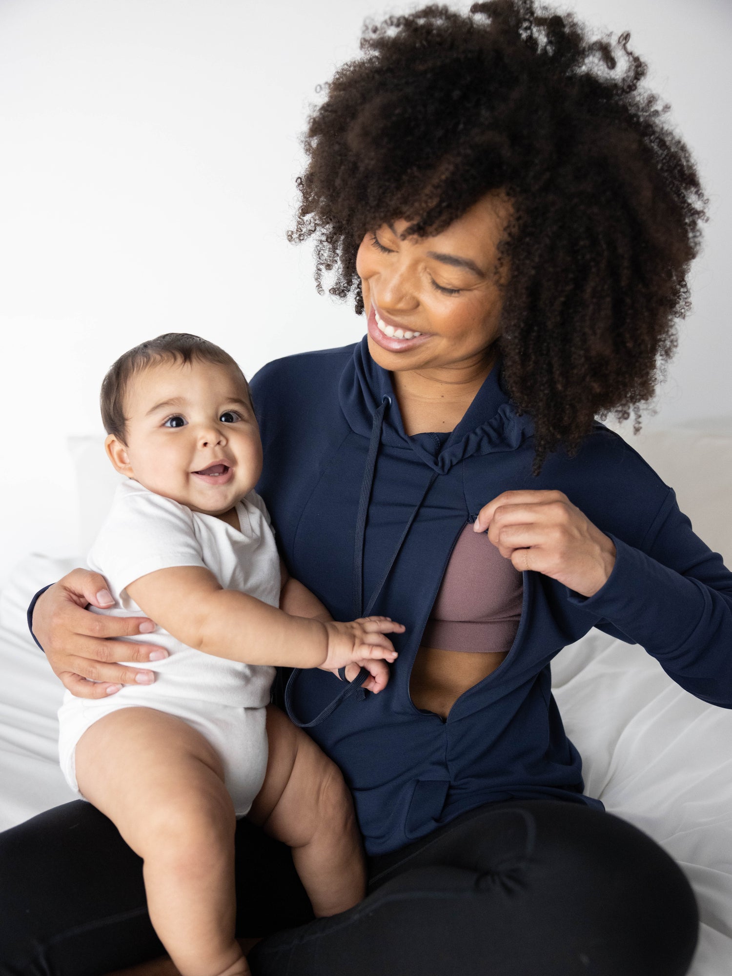 Front view of model wearing the Bamboo Maternity & Nursing Hoodie in Navy, showing zipper nursing access and holding baby on lap.