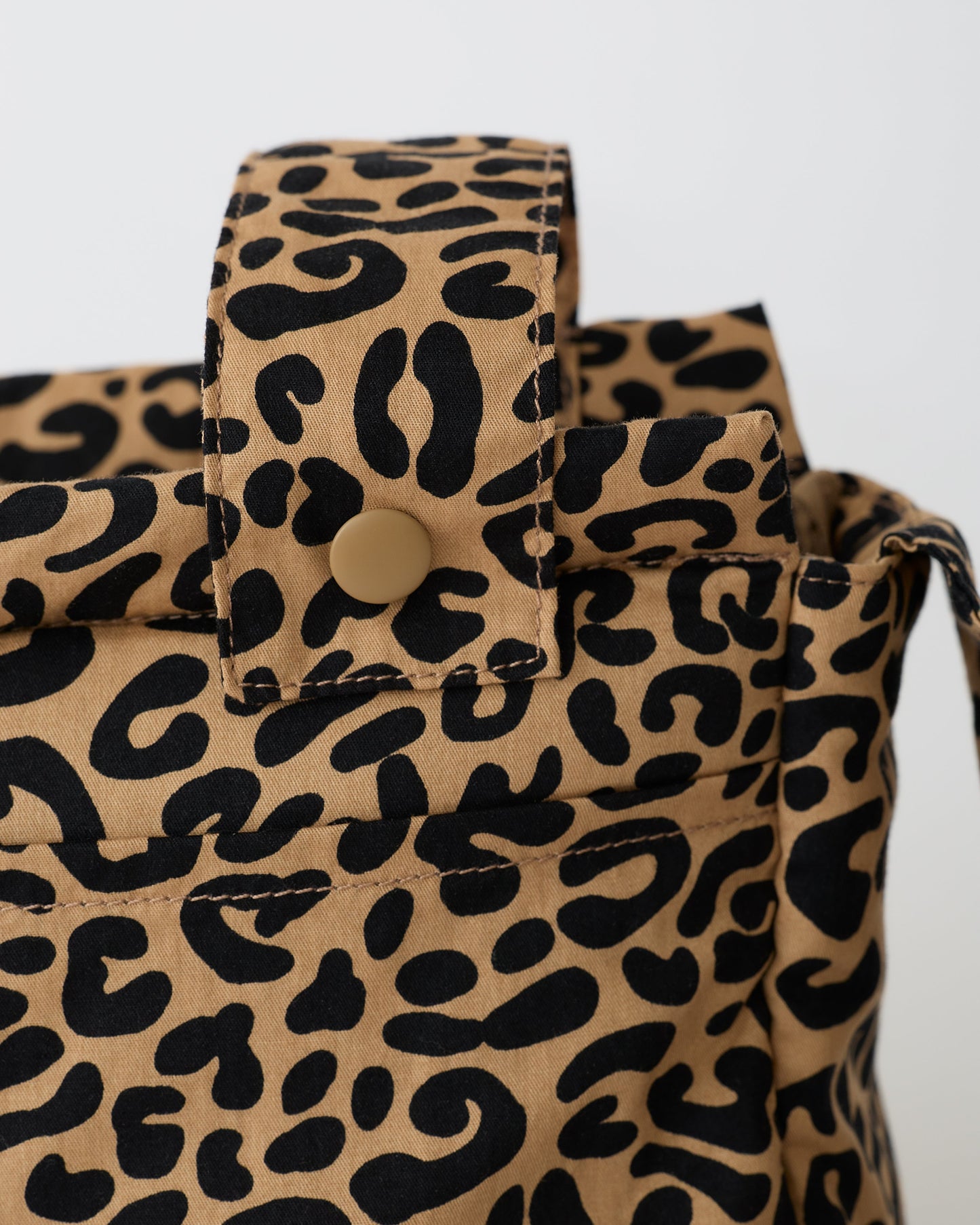 Close up of the snap and strap of the Stroller Party™ Caddy Bag in Leopard on a beige background.
