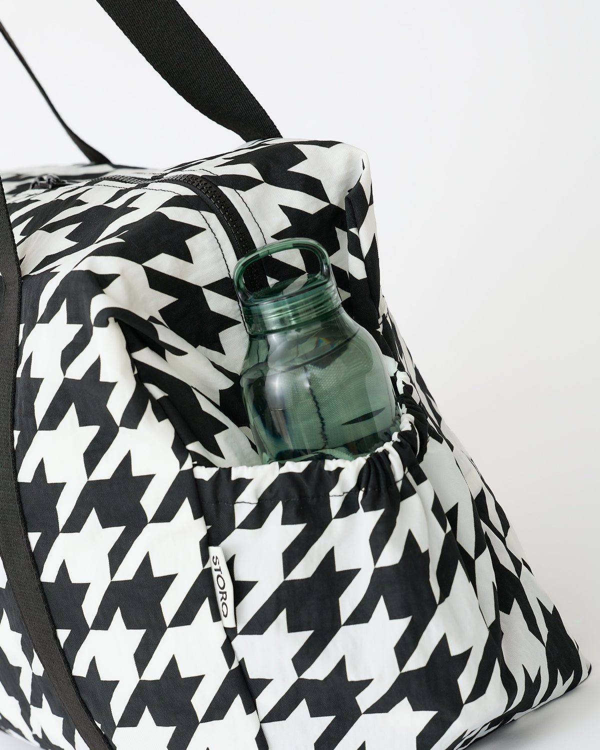 Close up of side pocket holding a water bottle, on the Large Weekender Bag in Black Houndstooth on an off white background.