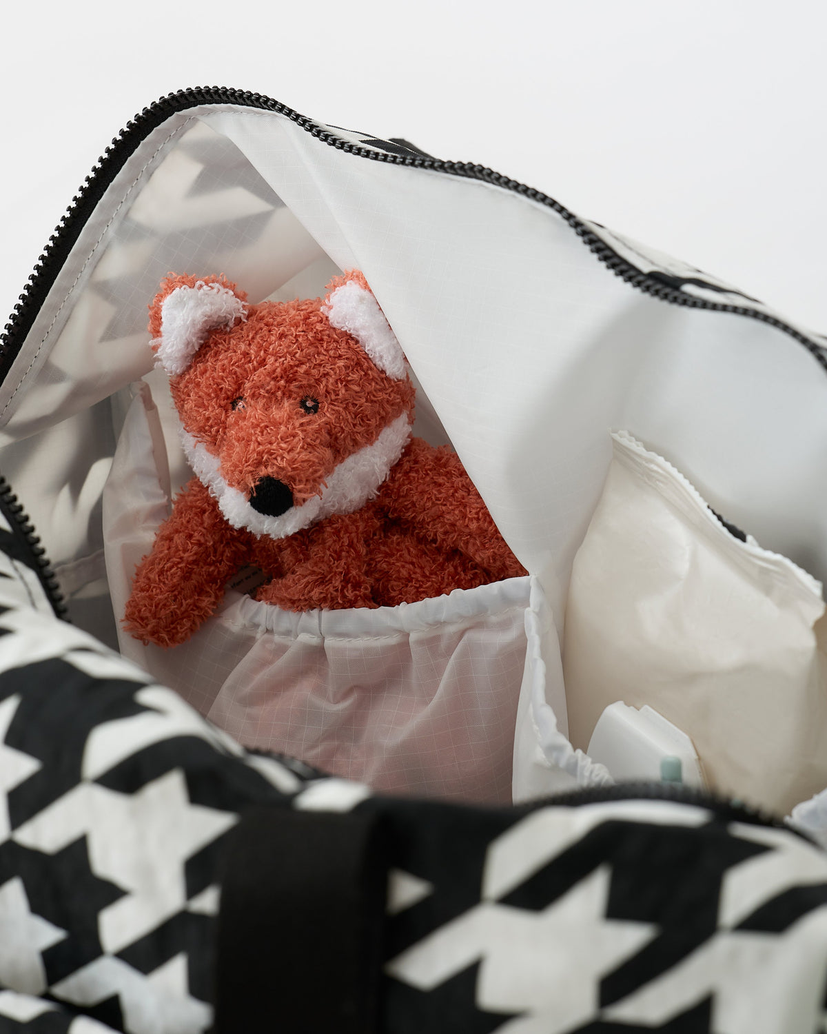 Close up of the interior, including several pockets, a lovey and wipes, all inside the Large Weekender Bag in Black Houndstooth on an off white background.