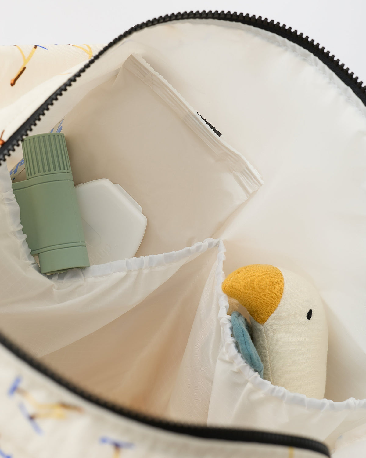 Close up on the interior, pockets, lovey, wipes and toys, inside the Large Weekender Bag in Ivory Ski, on an off white background.