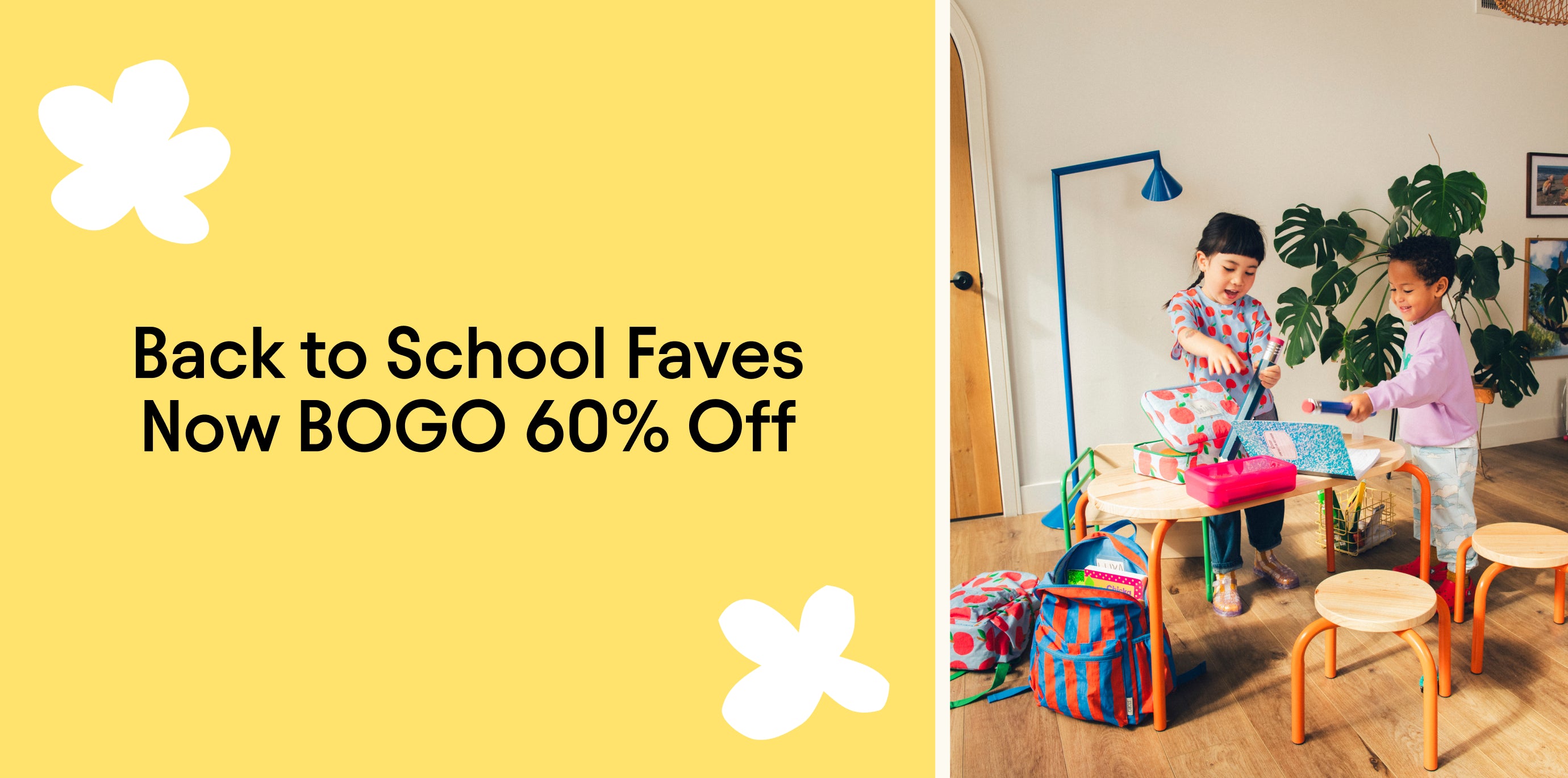 Promotional image with yellow background and white flower shapes and black text reading, Back to School Faves Now BOGO 60% Off. Image with two children playing in a play space with table, chairs, notebooks, oversized pencils, Cool Kid Backpacks, Cool Kid Lunch Boxes and Graphic Tee in Blue Apple.