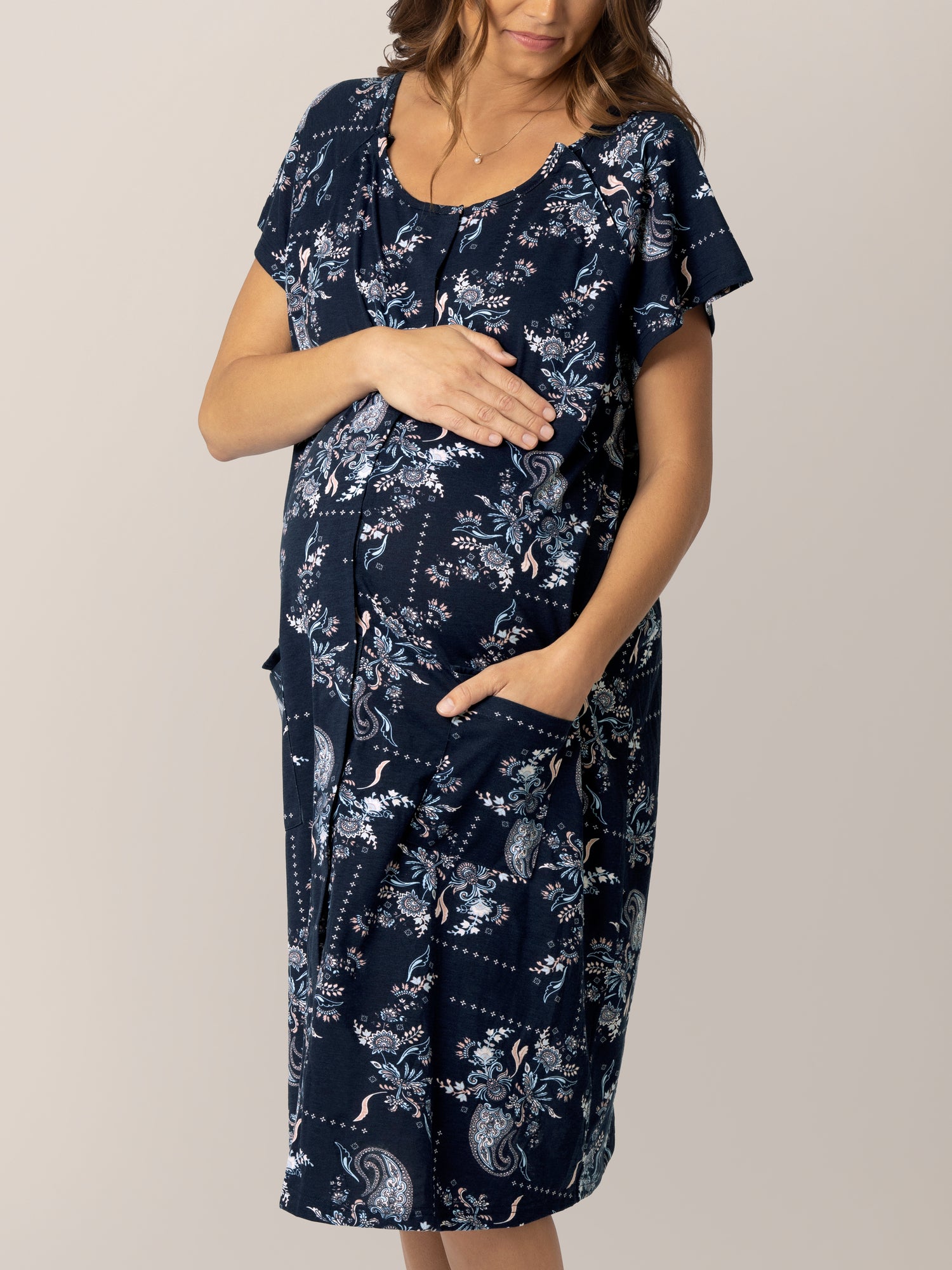 Cropped in front view of pregnant model wearing the Universal Labor & Delivery Gown in Navy Paisley, with one hand in pocket..