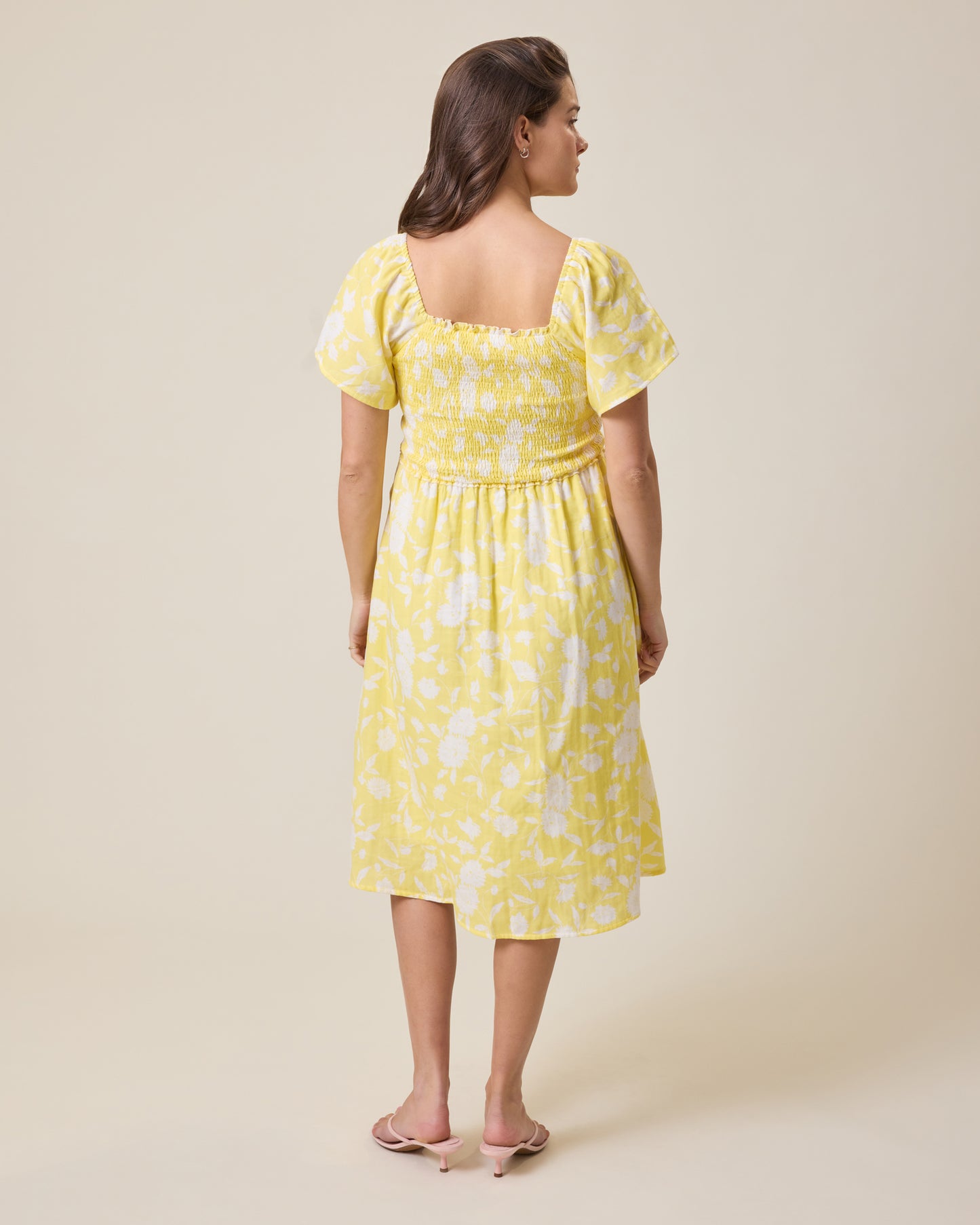 Woman wearing the Lola Smocked Maternity & Nursing Midi Dress in a Yellow Floral pattern against a plain background