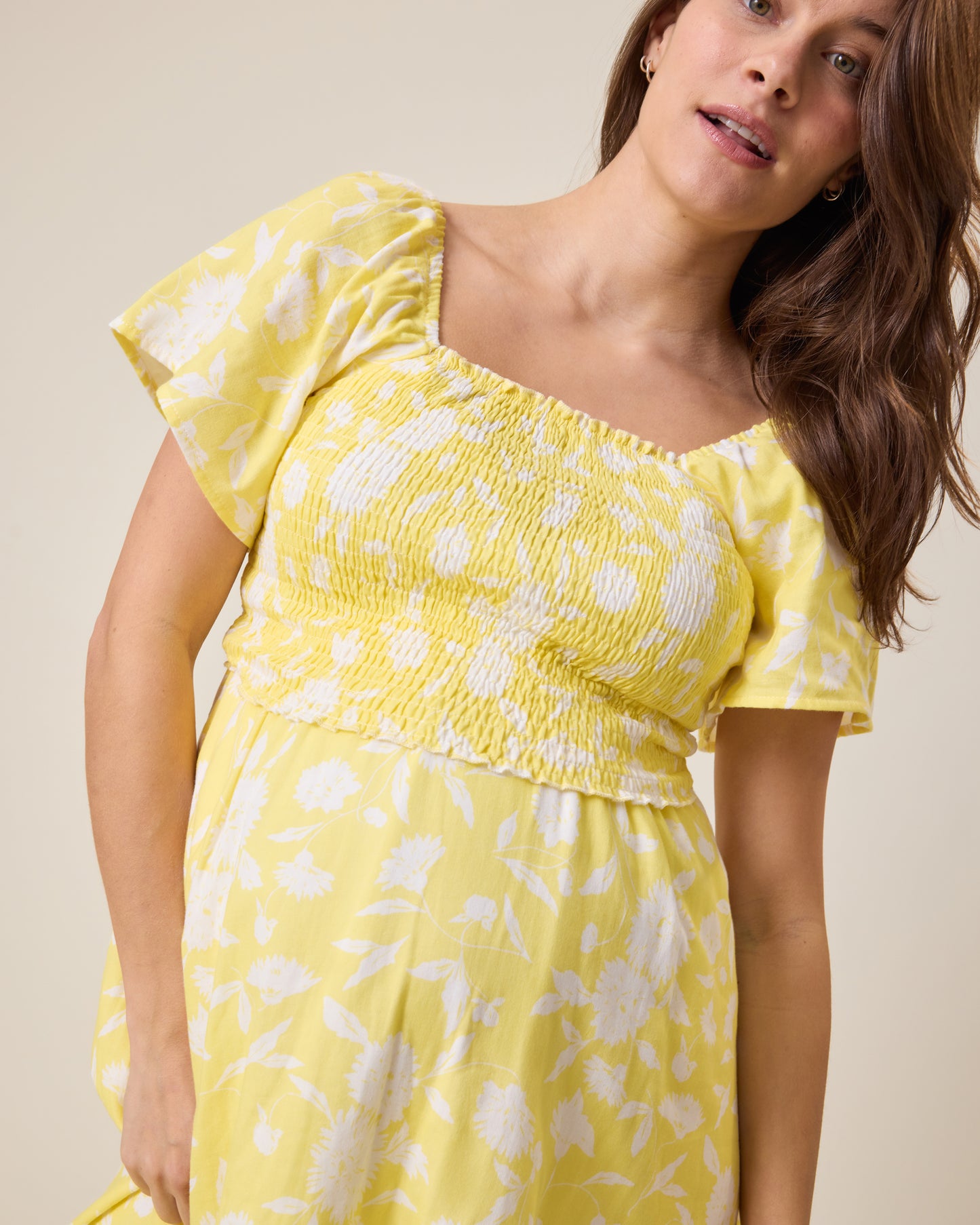 Woman wearing the Lola Smocked Maternity & Nursing Midi Dress in a Yellow Floral print against a neutral background