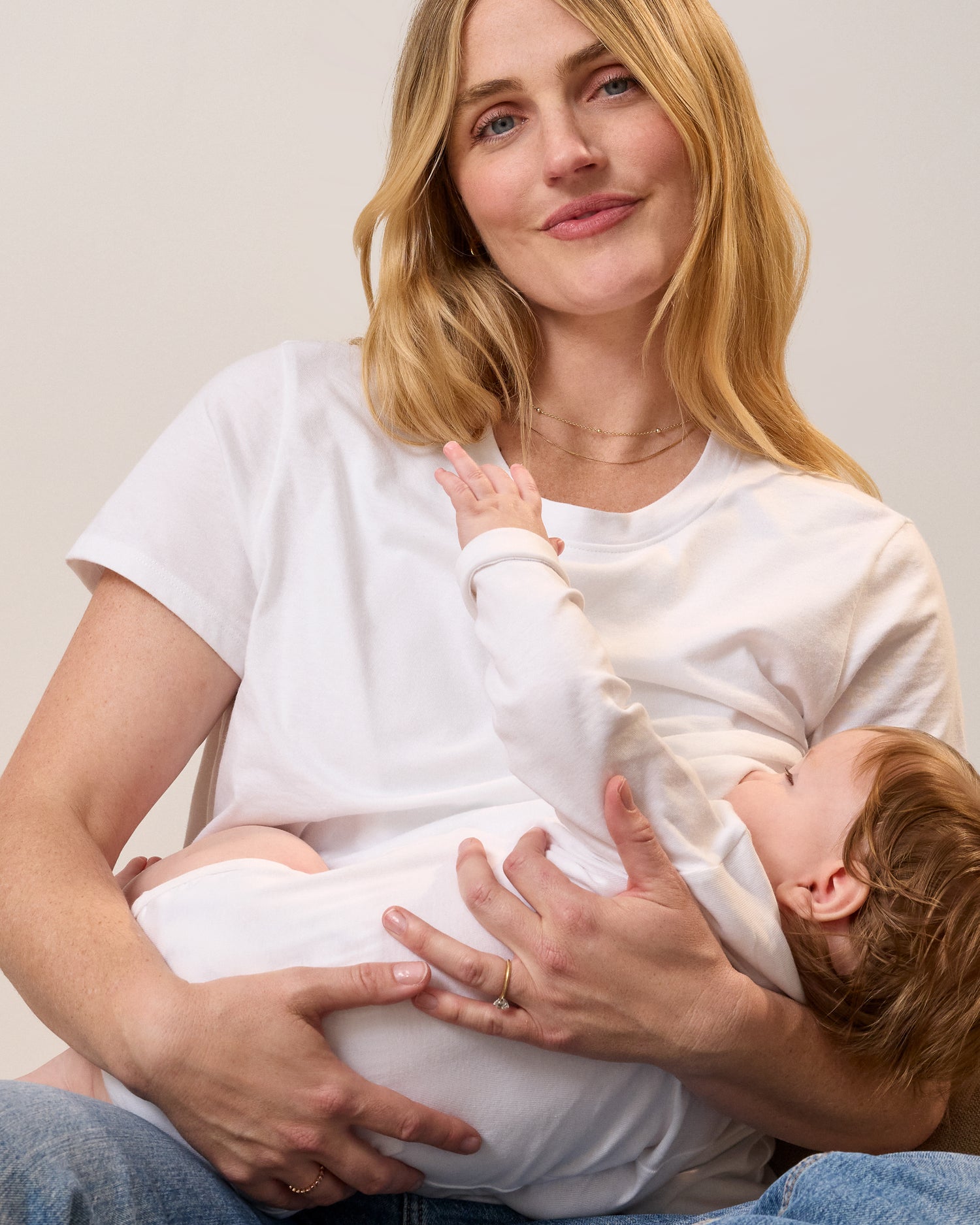 Model wearing Classic Cotton Nursing T-shirt in White on a neutral background nursing a baby