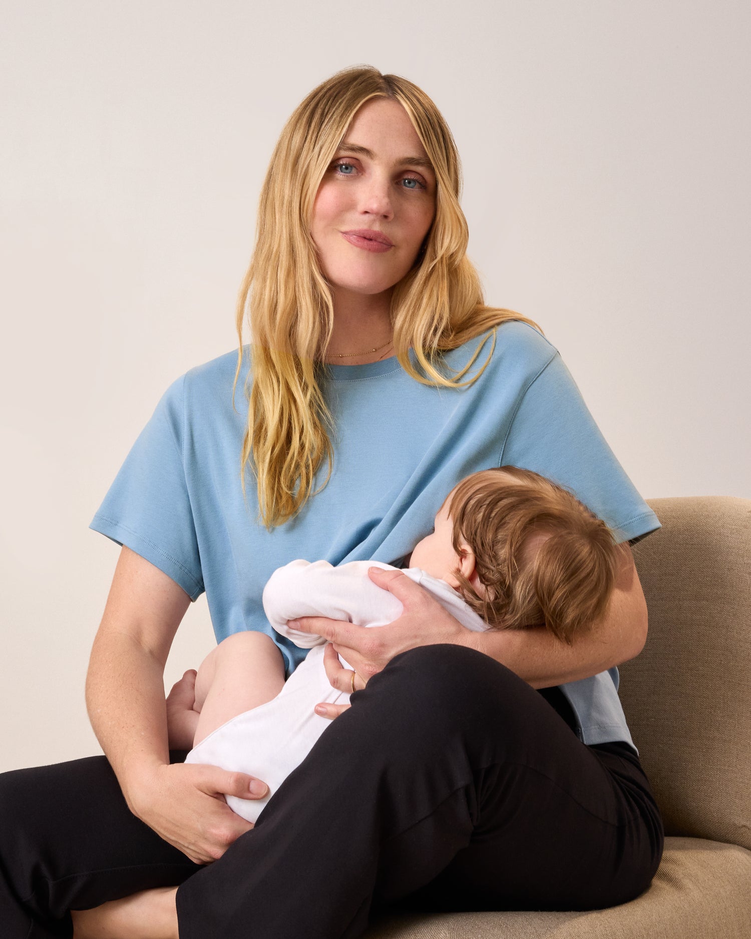 Model wearing Pima Cotton Side Zip Maternity & Nursing T-shirt in Vintage Blue sitting on a lounge chair, nursing