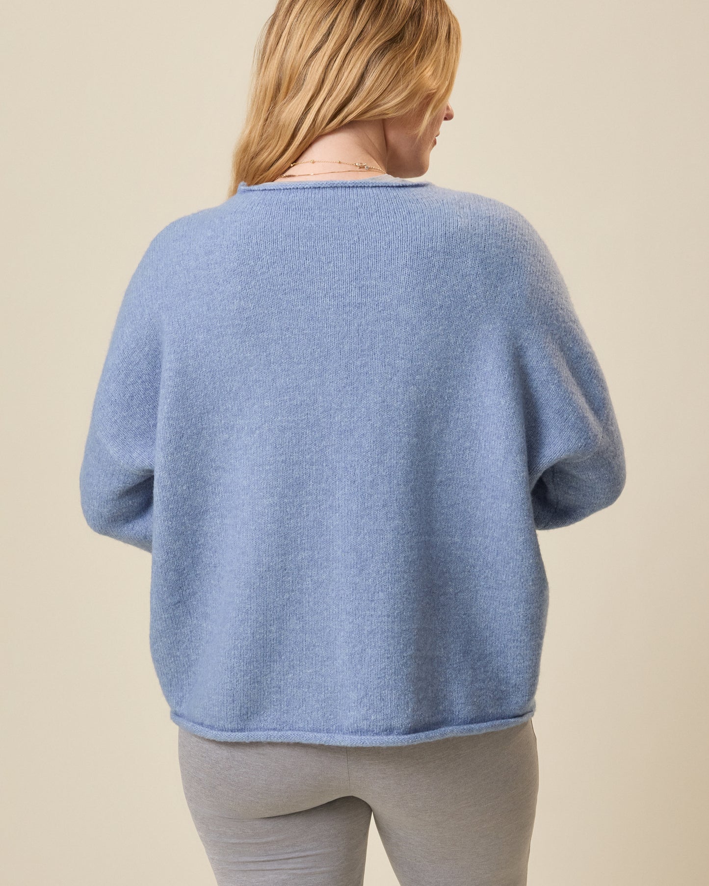 Person wearing a blue sweater and gray pants against a beige background