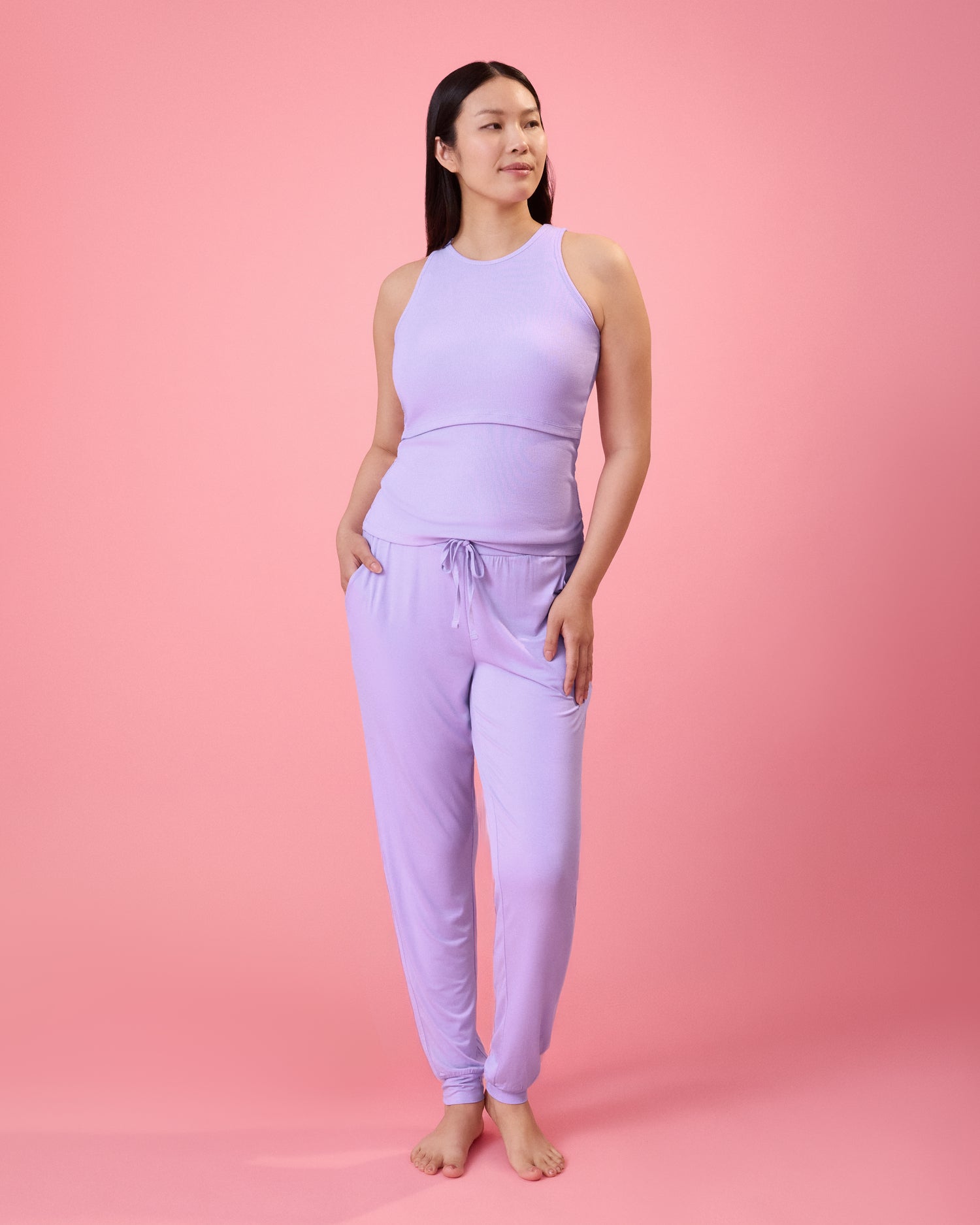 Front view of model wearing Ribbed Bamboo Racerback Nursing Tank in Lavender and Ultralight Sleep & Lounge Jogger in Lavender on a pink background
