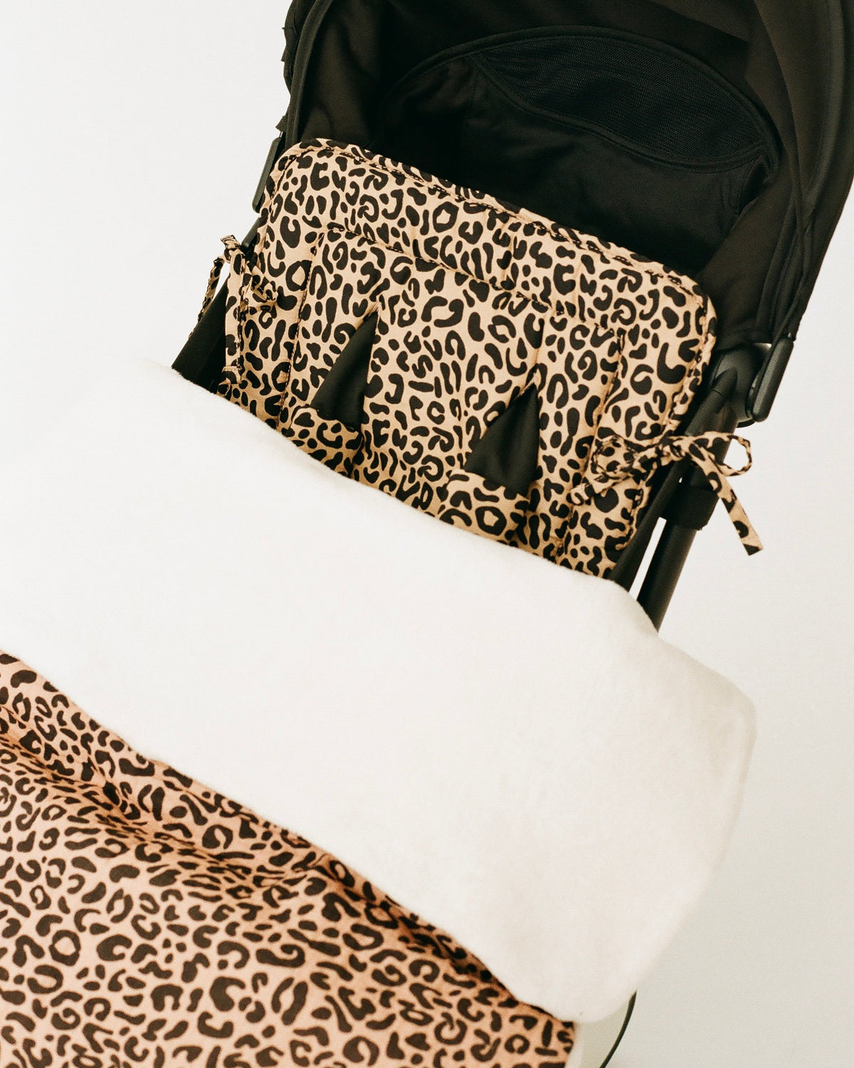 Cozy Stroller Blanket in Leopard and Stroller Party™ Seat Liner & Strap Covers in Leopard on a black stroller, on an off white background.