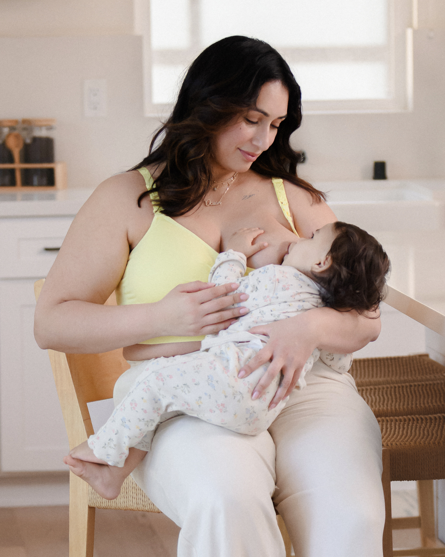 Model sitting in kitchen nursing baby and wearing the Sublime® Hands-Free Pumping & Nursing Bra Light Lemon @model_info:Connie is wearing an X-Large Busty.