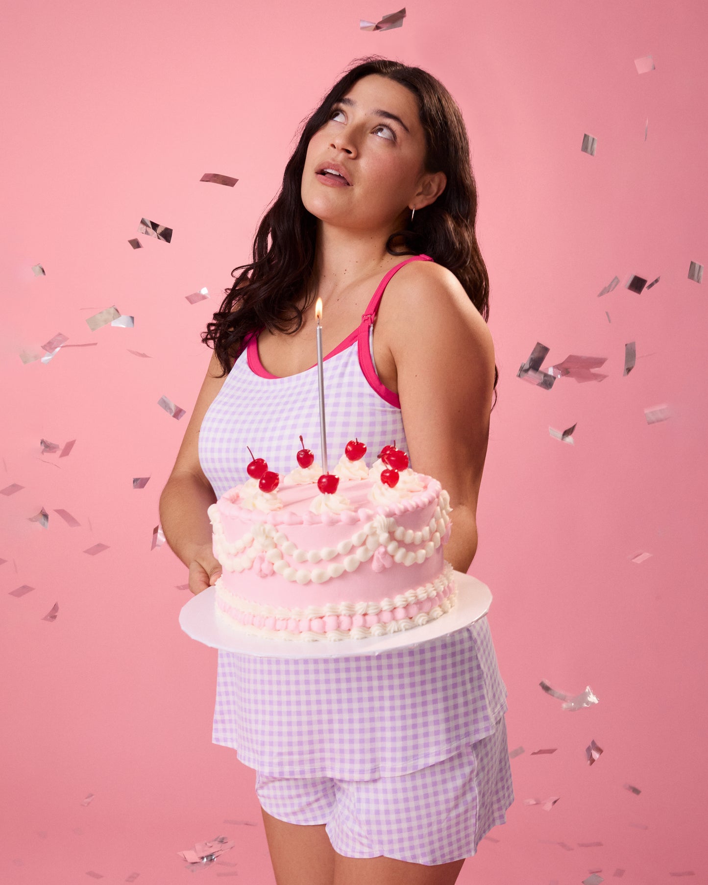 Model wearing Bamboo Maternity & Postpartum Lounge Short in Lavender Gingham holding a decorated pink cake on a pink background with confetti falling around her