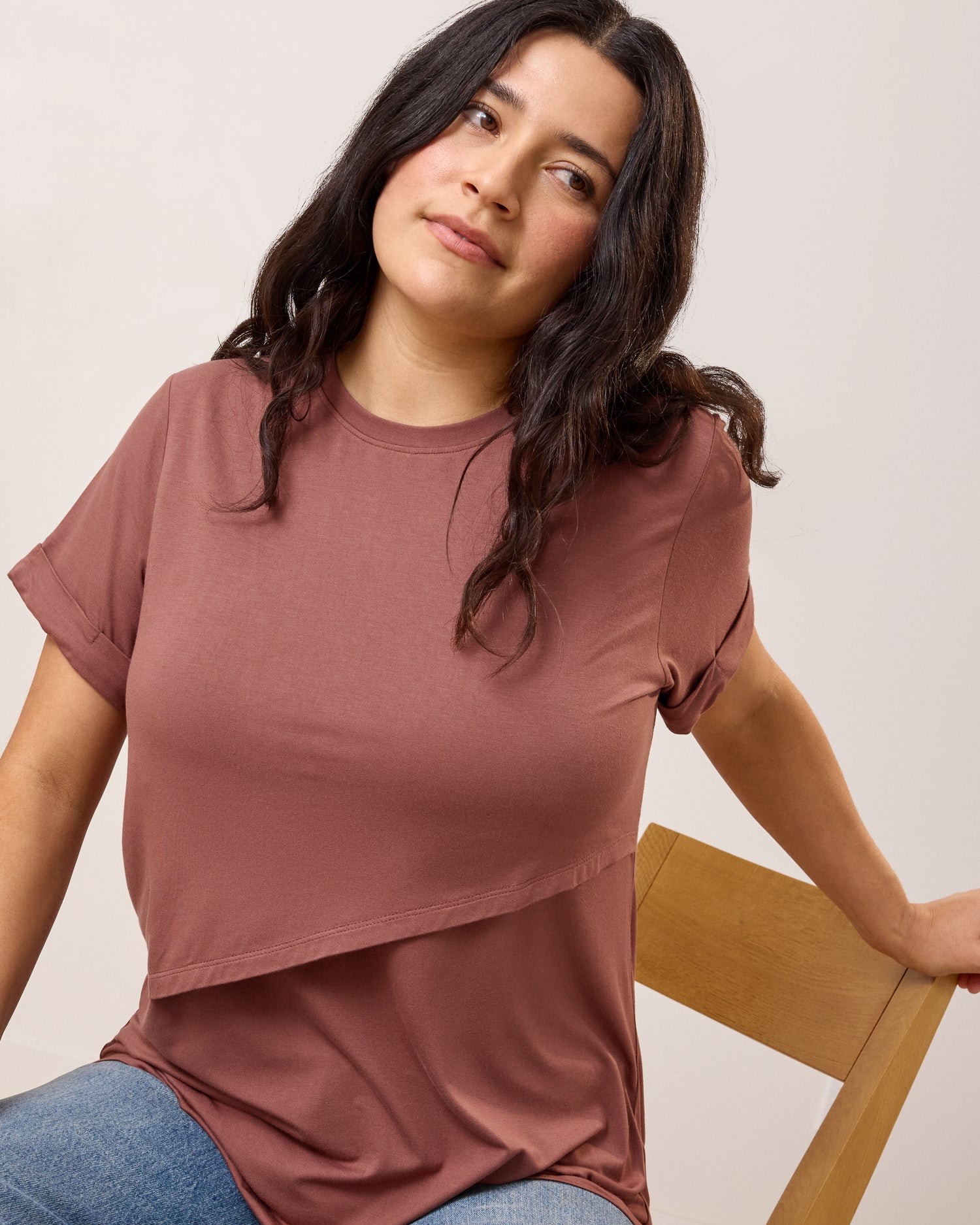 Model wearing the Asymmetrical Nursing T-shirt in Redwood sitting on a wooden chair