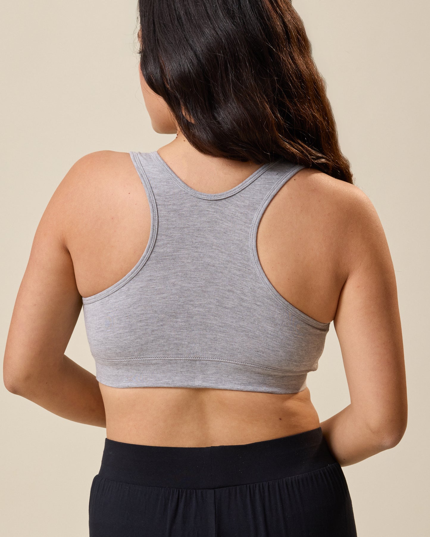 Person wearing the French Terry Racerback Nursing Bra in grey heather and black pants on a beige background
