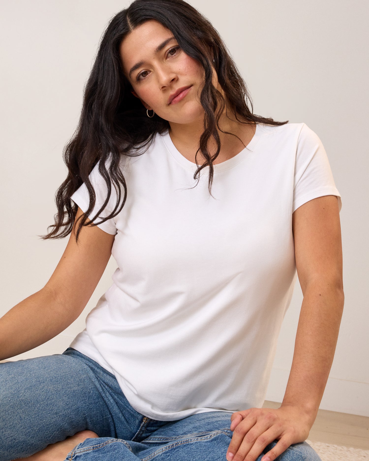 Front view of model wearing Slim Fit Modal Nursing T-shirt in White on a neutral background, sitting on the floor in a relaxed posed