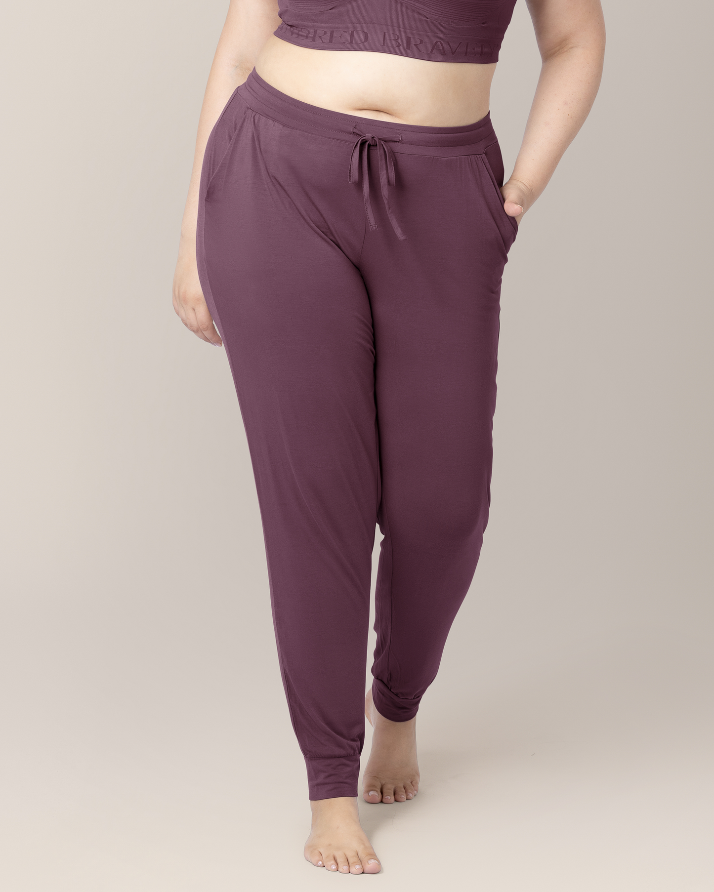 Cropped in front view of model wearing the Everyday Lounge Jogger in Burgundy Plum, with one hand in pocket, highlighting waistband and drawstring