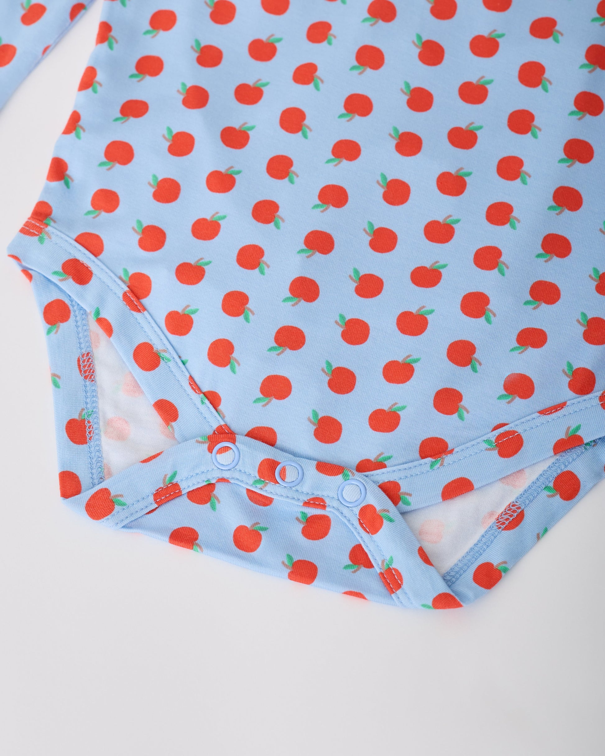 Close up of the snaps on Blue Apple Onesie of the Long Sleeve Bamboo Onesie Two-Pack in Apple pattern on a gray background.