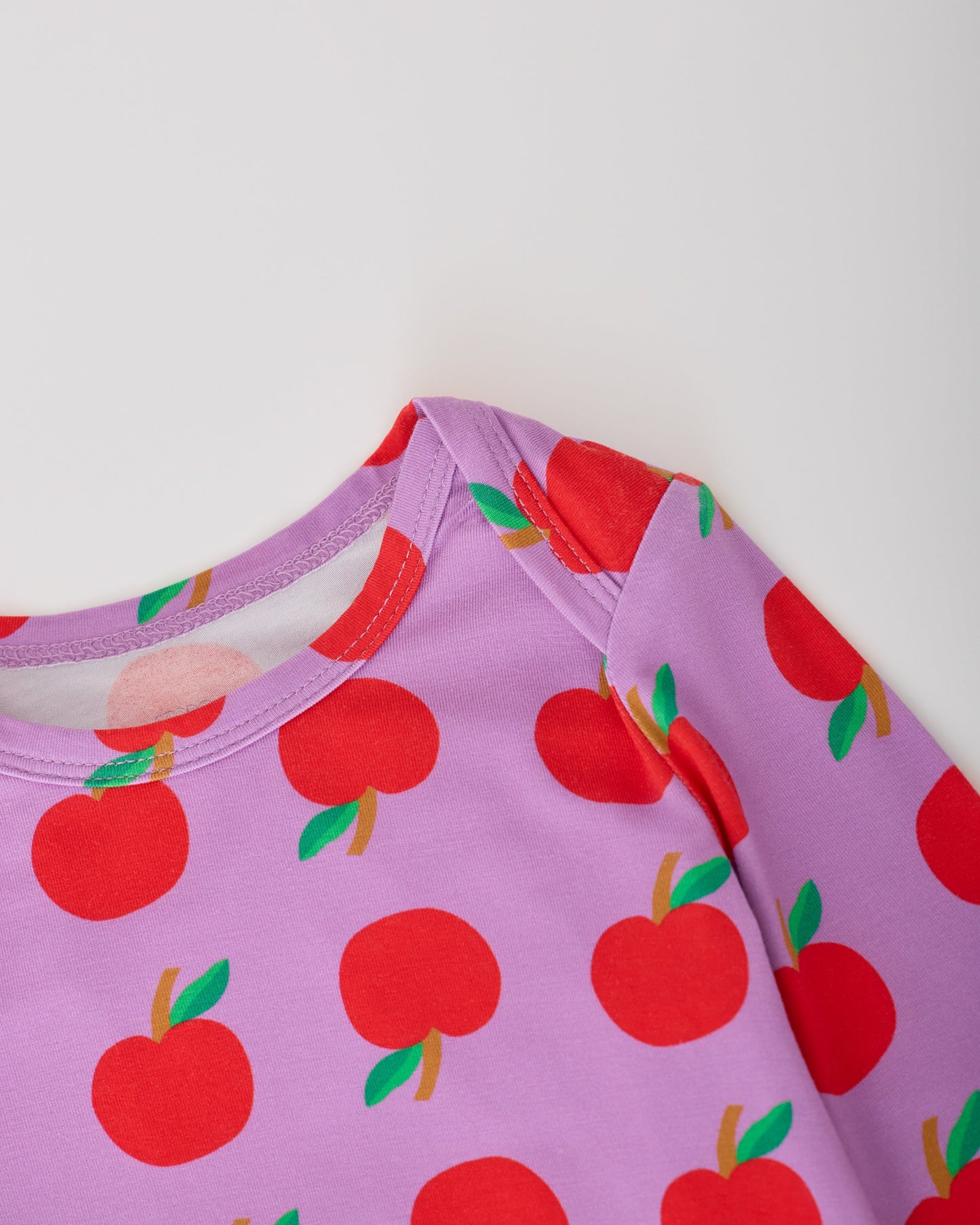 Close up of the collar on the Purple Apple Onesie of the Long Sleeve Bamboo Onesie Two-Pack in Apple pattern on a gray background.