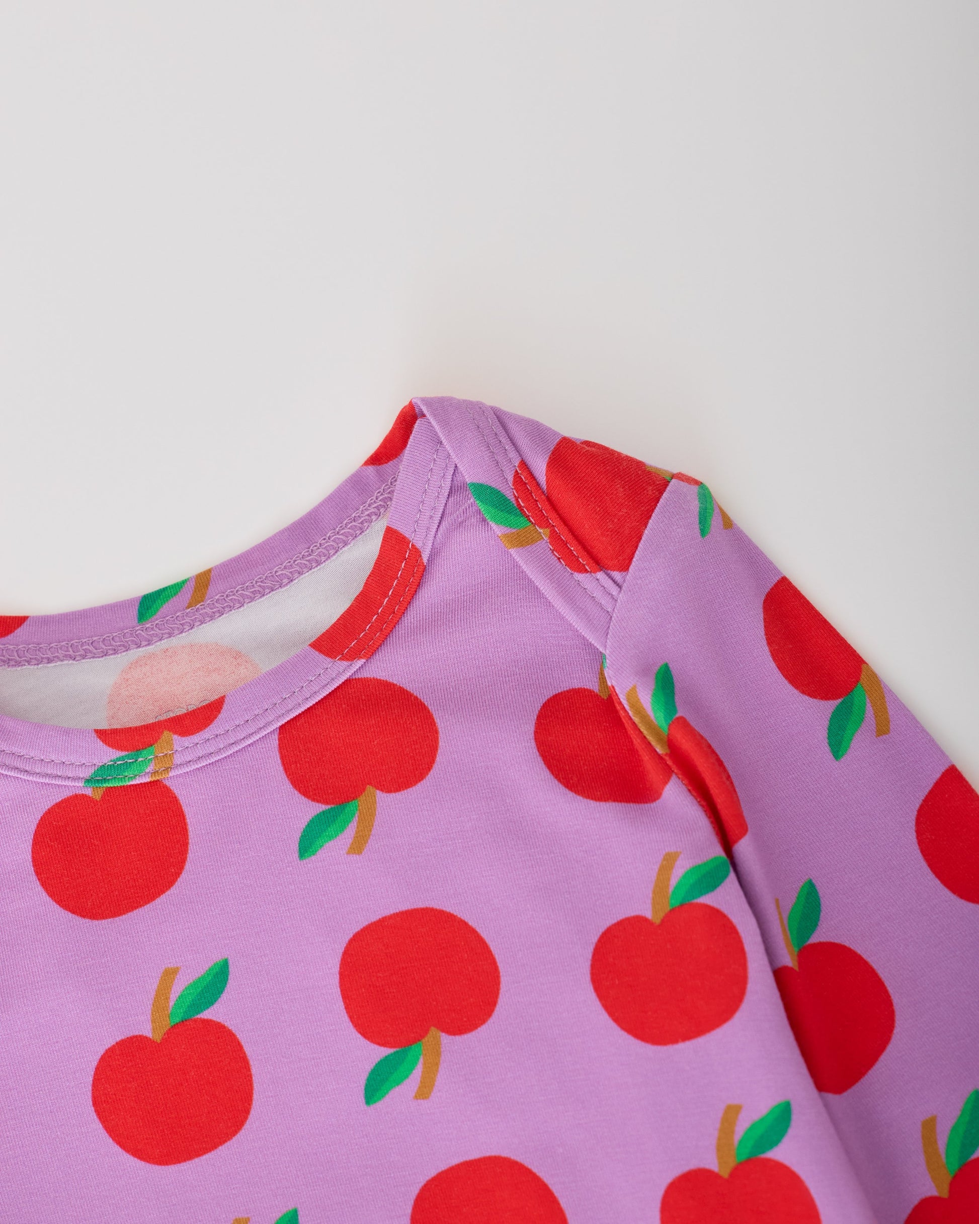 Close up of the collar on the Purple Apple Onesie of the Long Sleeve Bamboo Onesie Two-Pack in Apple pattern on a gray background.