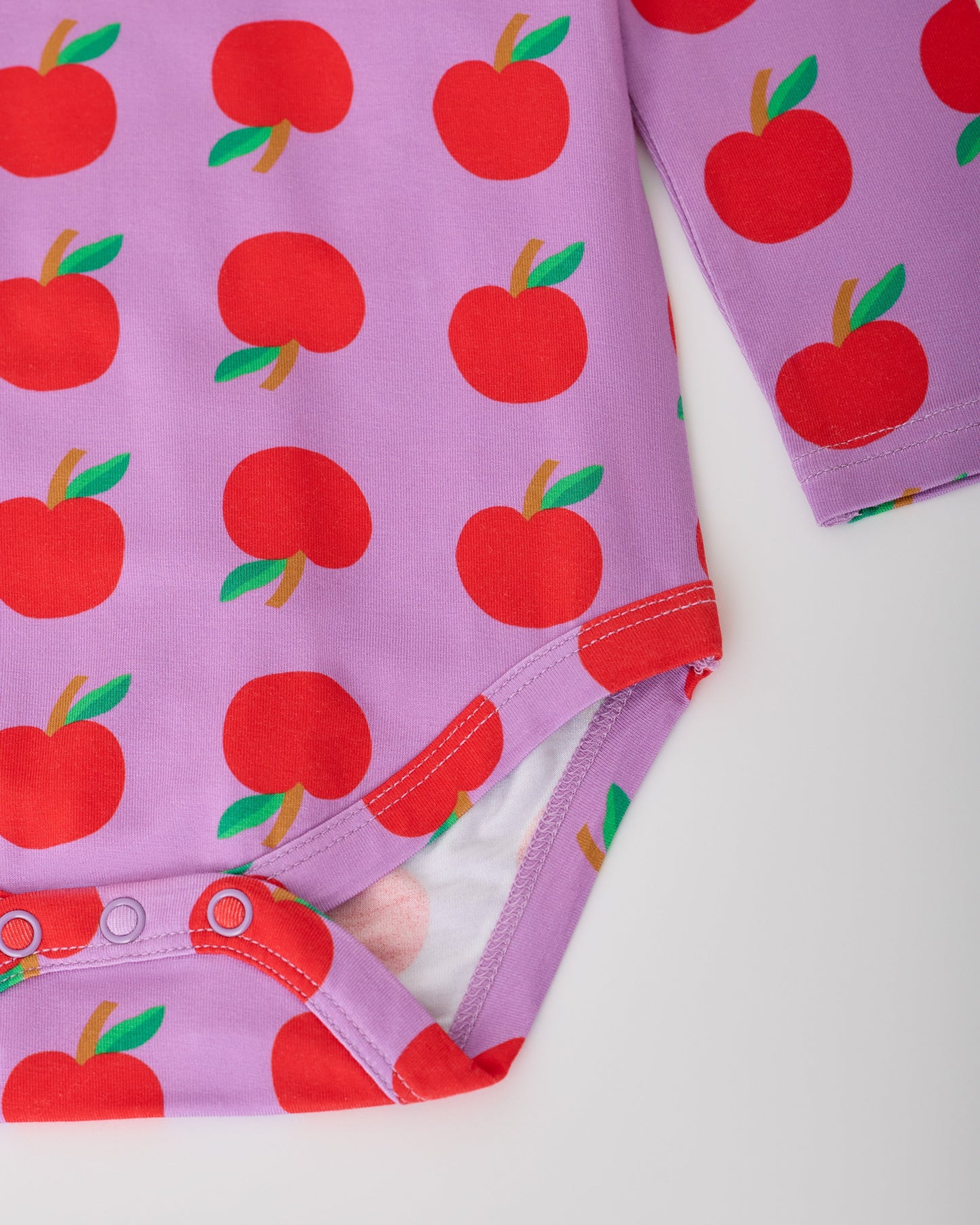 Close up of the snaps on the Purple Apple Onesie of the Long Sleeve Bamboo Onesie Two-Pack in Apple pattern on a gray background.