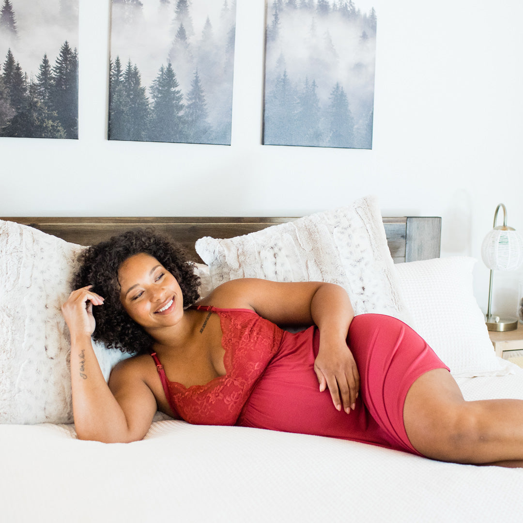 Pregnant model laying on a bed wearing the Lucille Maternity & Nursing Nightgown in Crimson. @model_info:Janalyn is 5'8" and wearing a Medium.