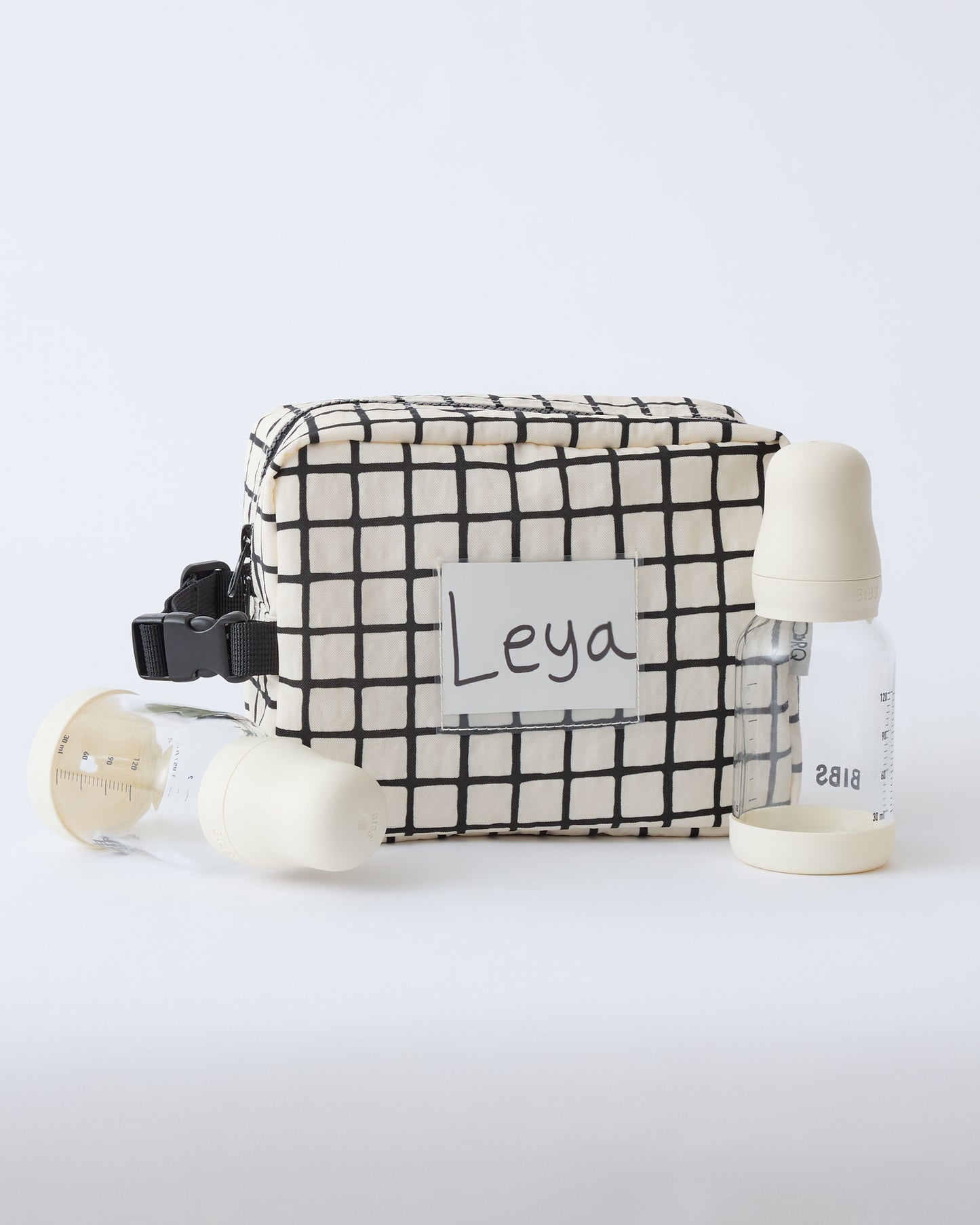 Mini Cooler Bag in Black Grid, with two milk bottles and a name tag inside the name tag pocket, on a beige background.