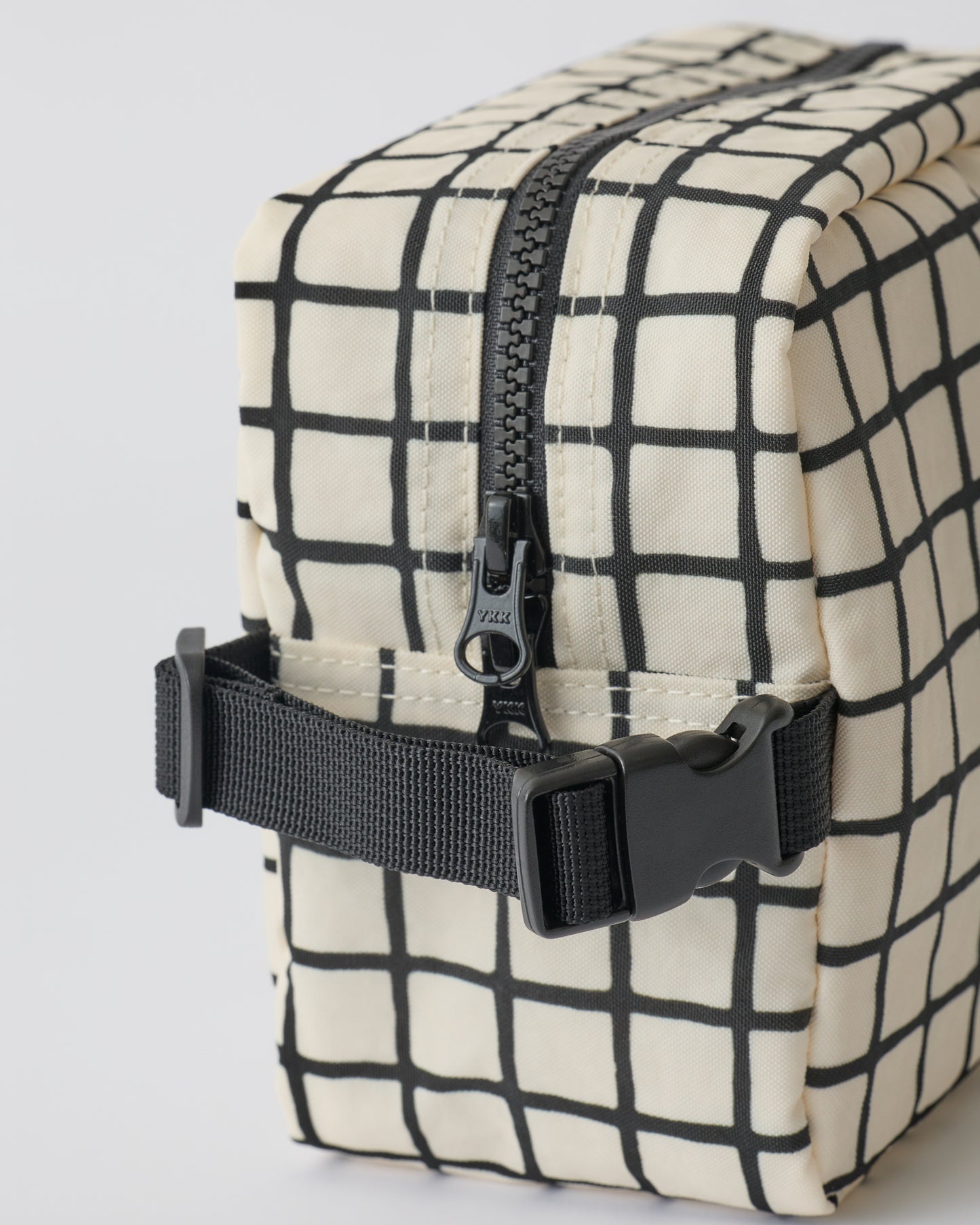 Close up of the zipper and handle of the Mini Cooler Bag in Black Grid, on a beige background.