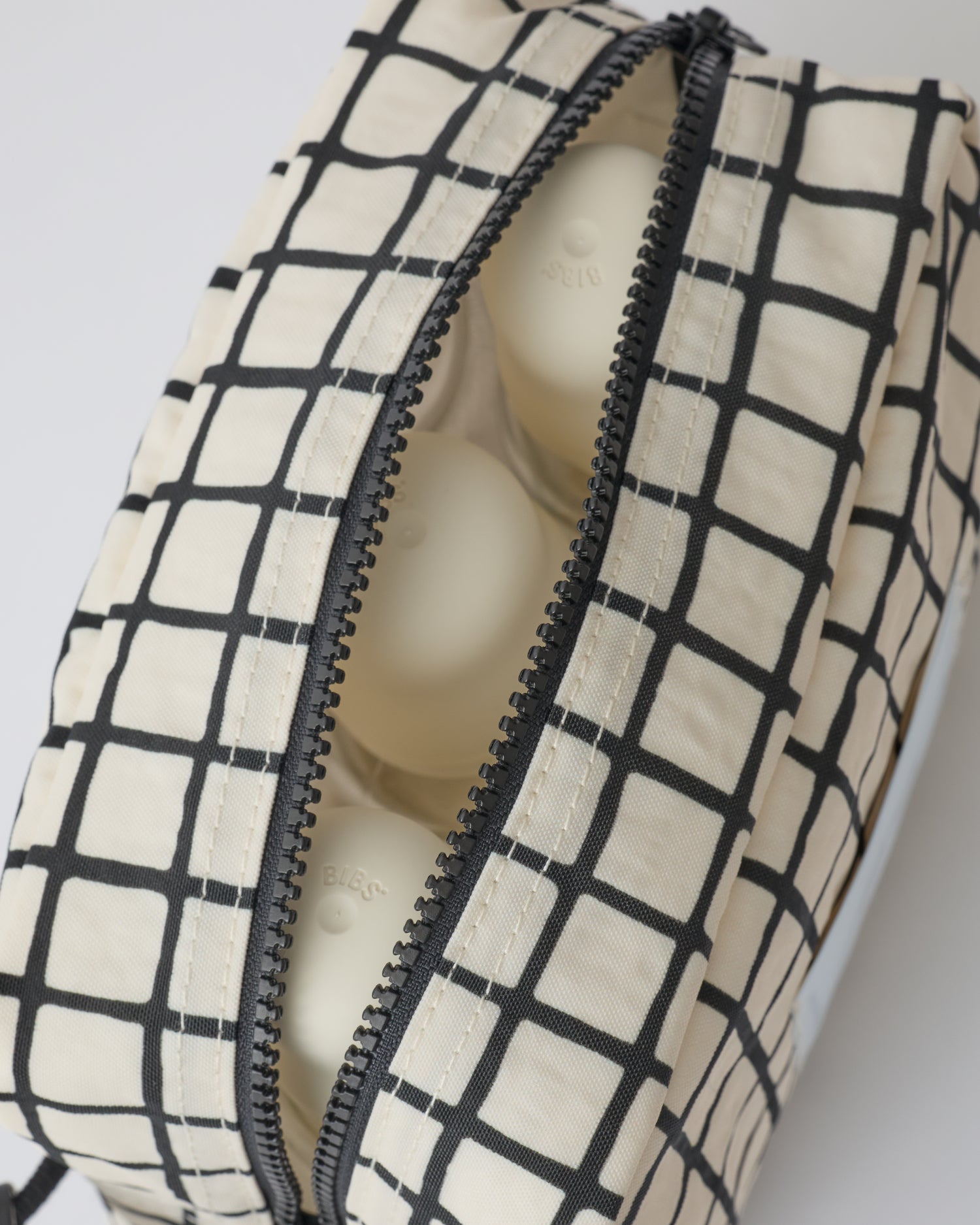 Close up of the zipper and interior of the Mini Cooler Bag in Black Grid, on a beige background.