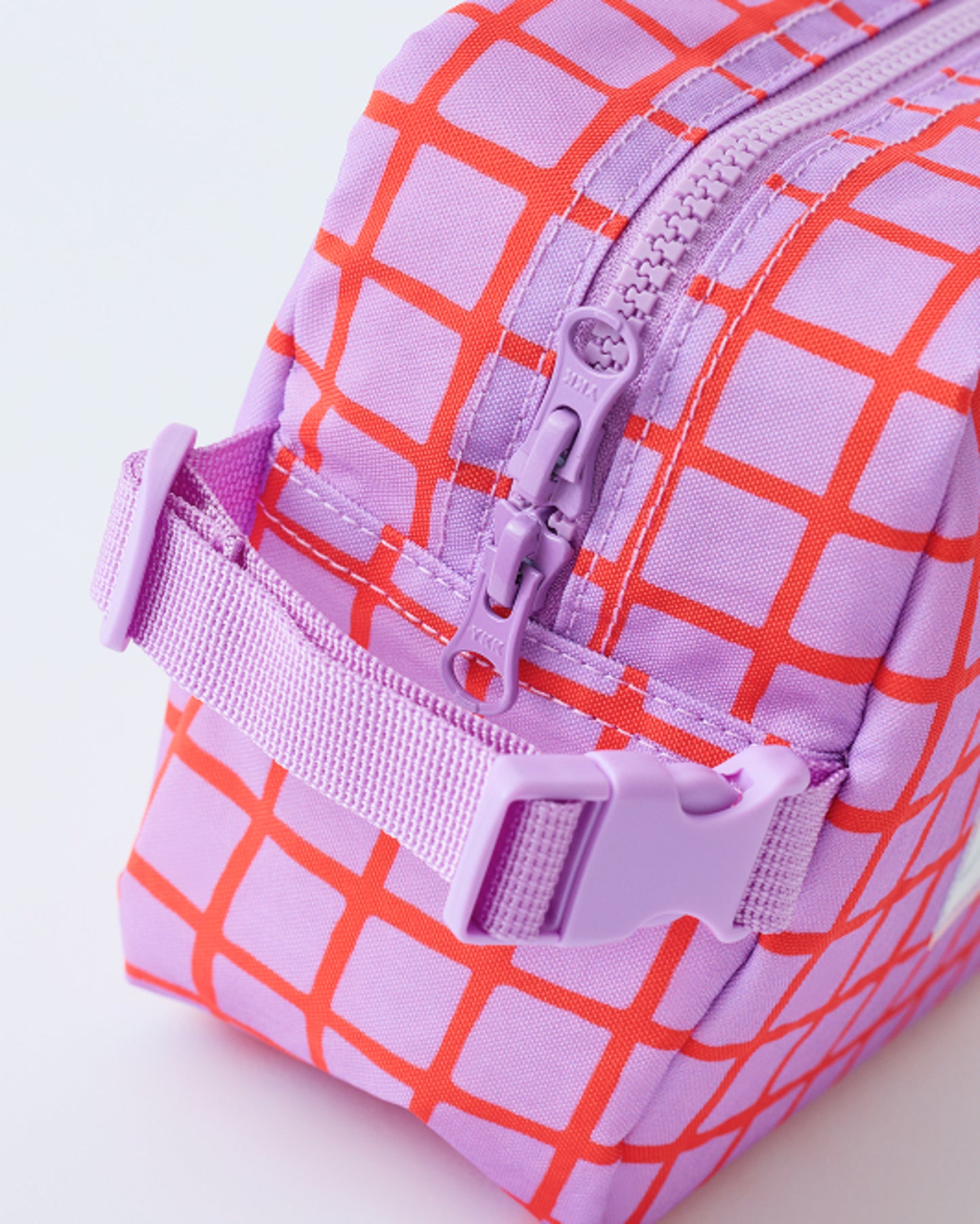 Close up of the zipper and clip of the Mini Cooler Bag in Orchid Grid, on a beige background.