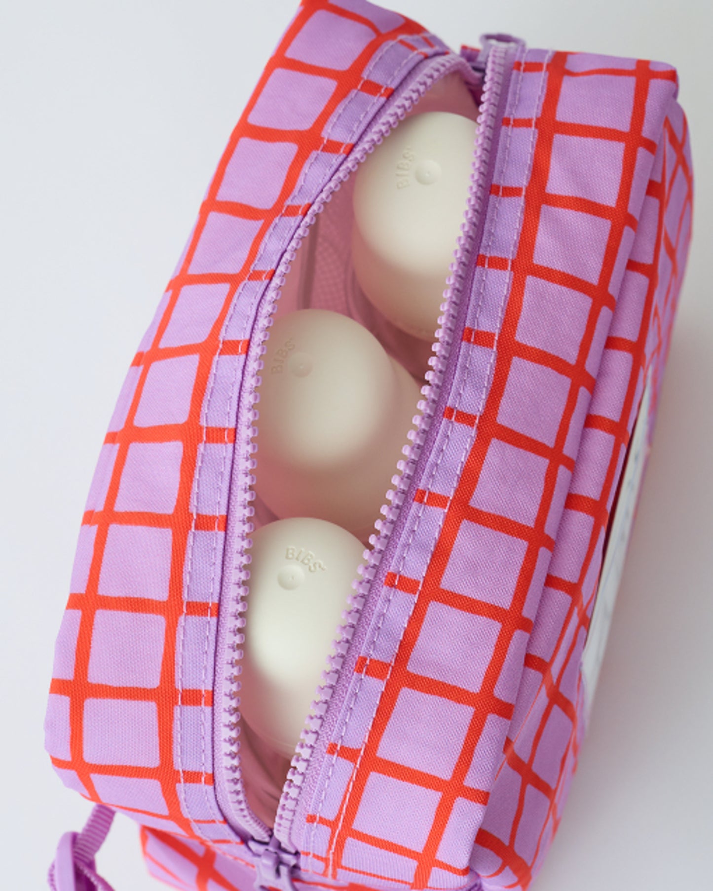 Close up of the zipper and interior with three milk bottles of the Mini Cooler Bag in Orchid Grid, on a beige background.