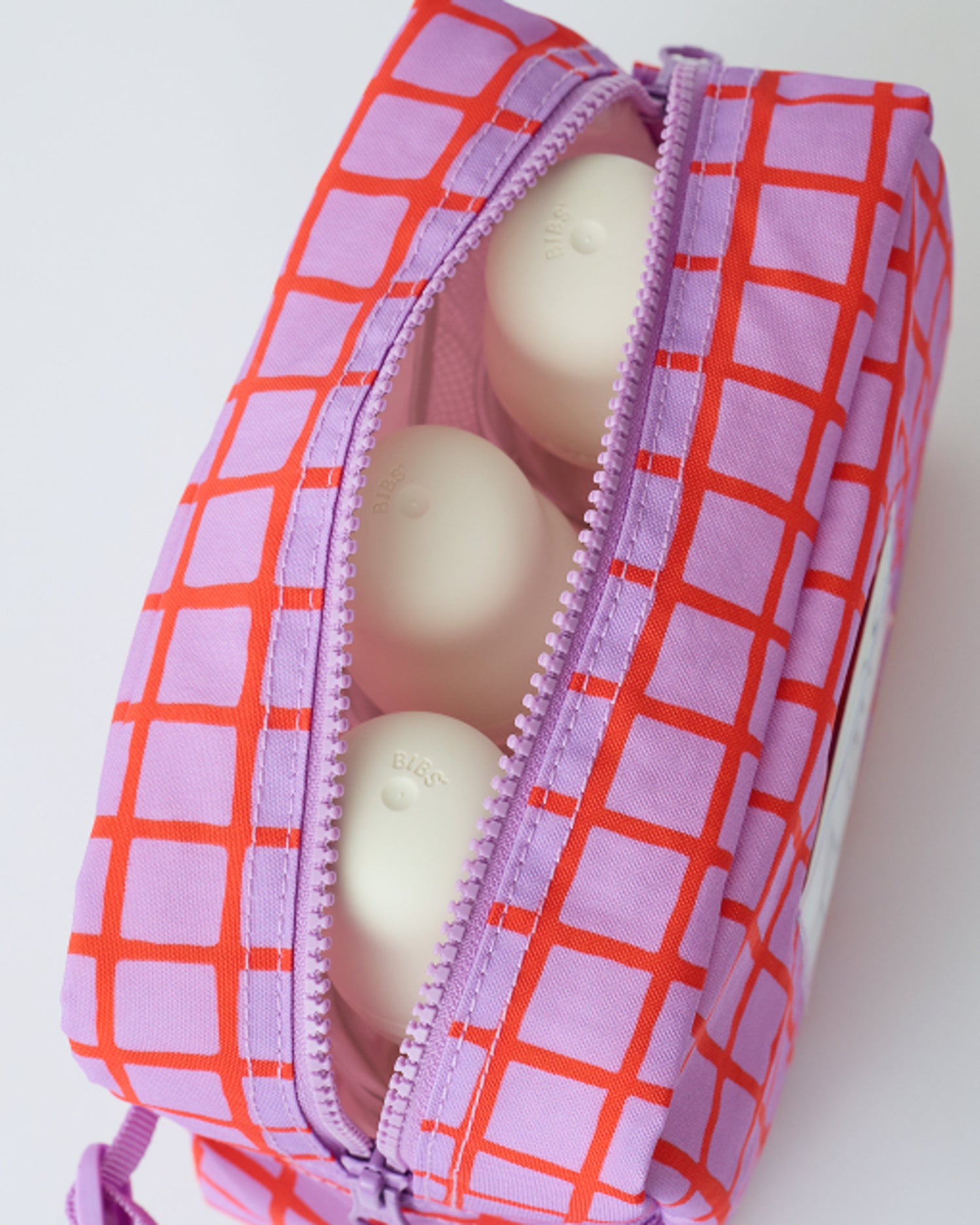 Close up of the zipper and interior with three milk bottles of the Mini Cooler Bag in Orchid Grid, on a beige background.