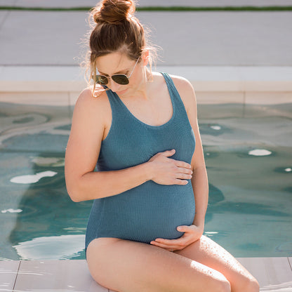 Model sitting by the pool while wearing the Crinkle Maternity One Piece Swimsuit @model_info:Kaitlyn is wearing a Small.