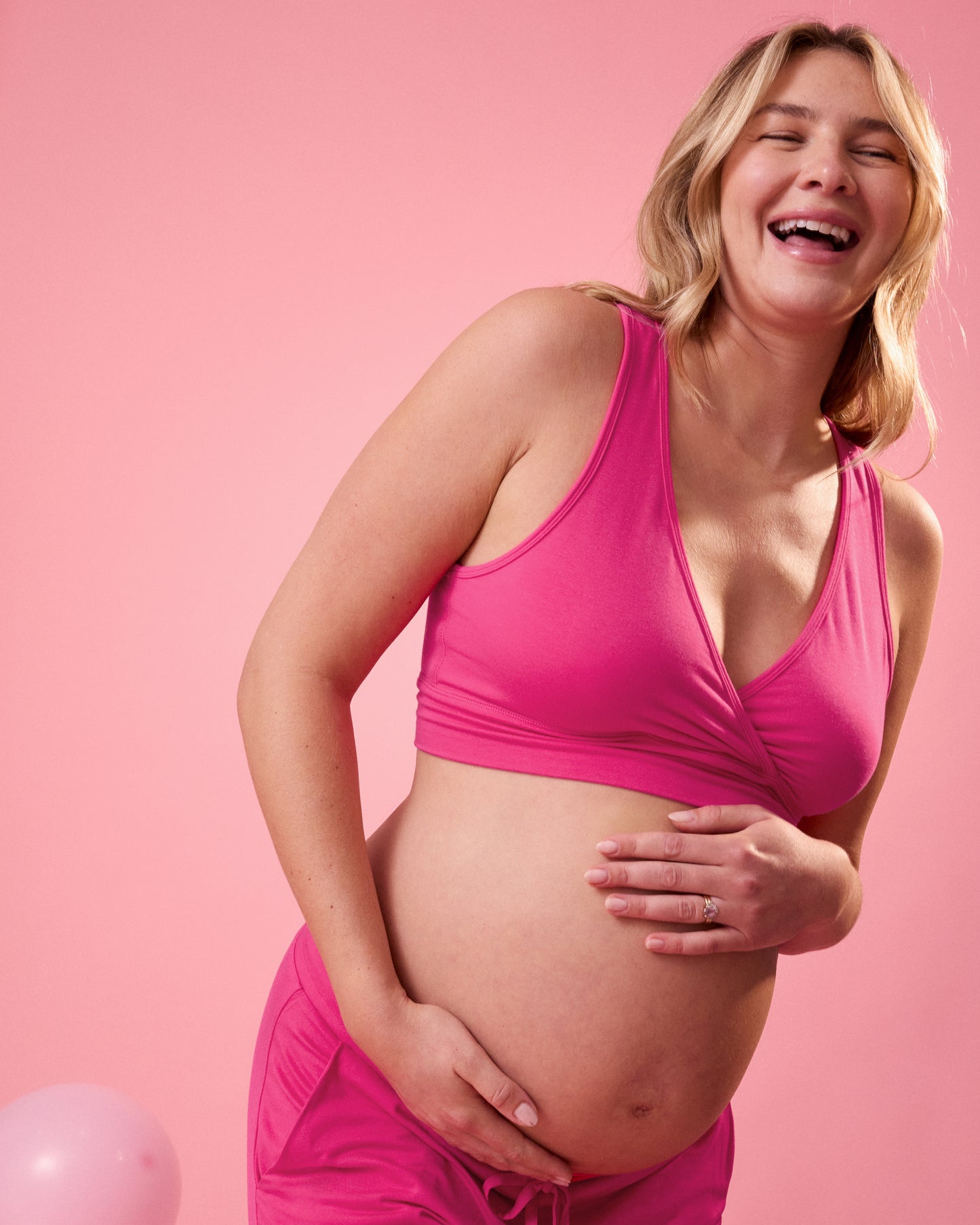 Front view of model wearing French Terry Racerback Nursing & Sleep Bra in Raspberry Pink on a pink background holder her pregnant belly
