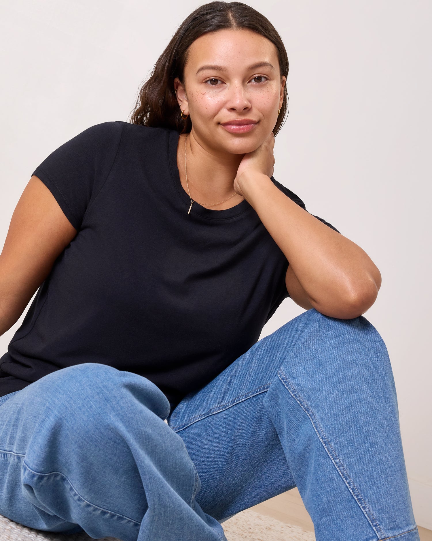 Model wearing Slim Fit Modal Nursing T-shirt in Black sitting on the floor in a relaxed posed on a neutral background
