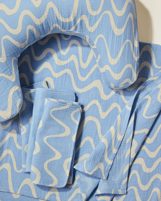 Set of blue and white wave patterned nursing pillow, burp cloths and swaddle  on a light background