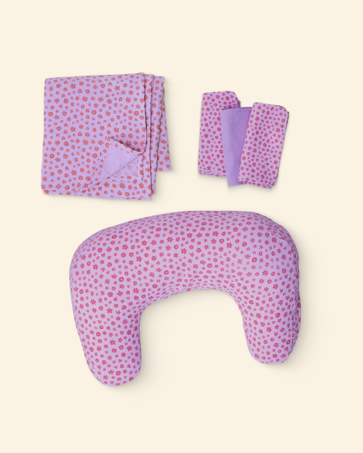 Set of lavender floral patterned nursing pillow, burp cloths, and swaddle on a light background